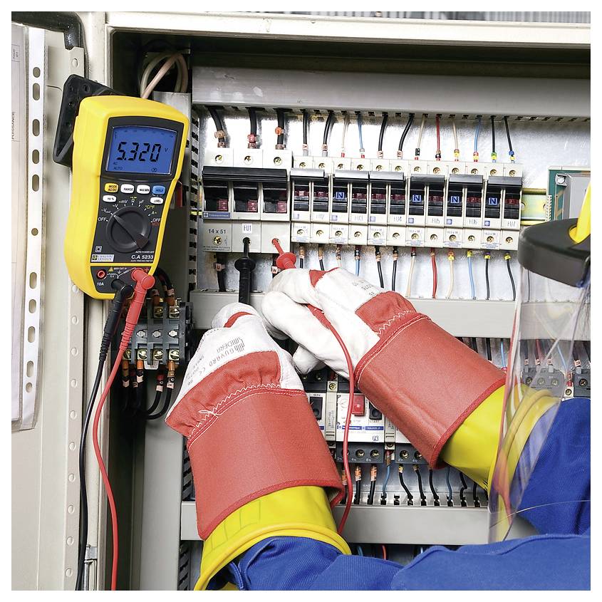 Elektriker mit Schutzkleidung benutzt ein Multimeter, um Spannung in einem geöffneten Schaltschrank zu messen.