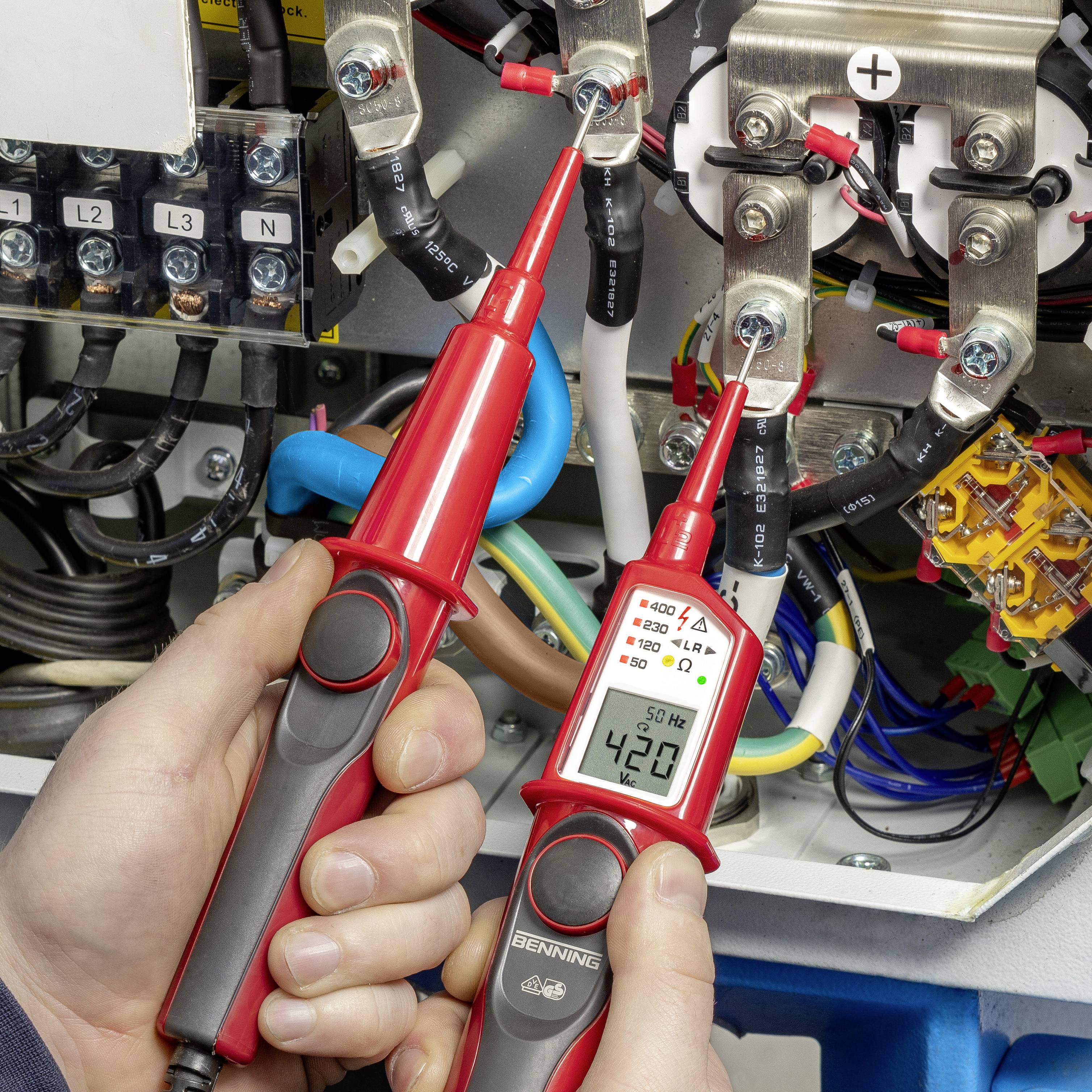 Eine Person misst mit einem Multimeter die Spannung an einem elektrischen Schaltkasten. Das Multimeter zeigt 420 Volt.