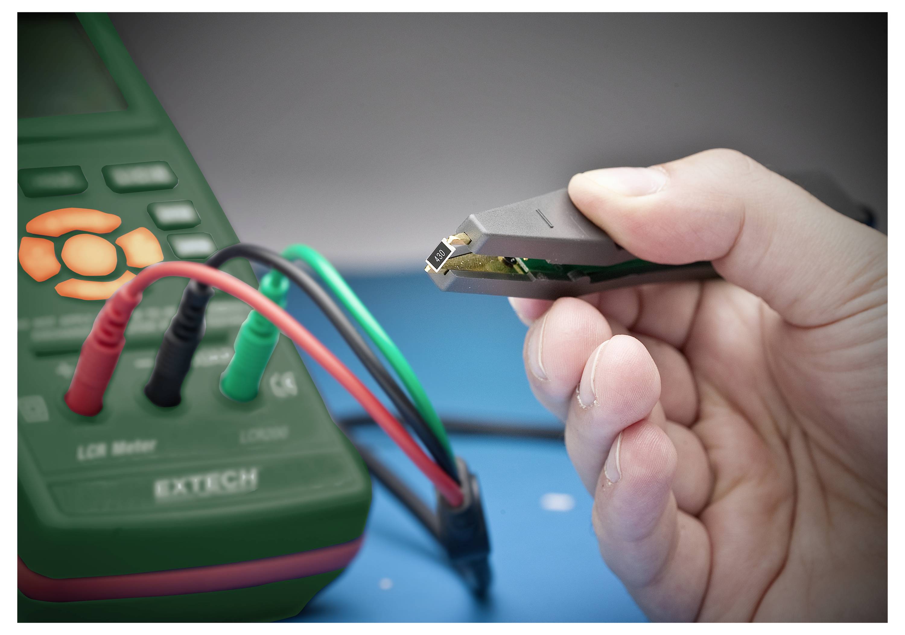 Eine Person, die eine elektronische Komponente mit einer Pinzette hält, testet diese mit einem digitalen LCR-Messgerät, das durch Messleitungen verbunden ist.