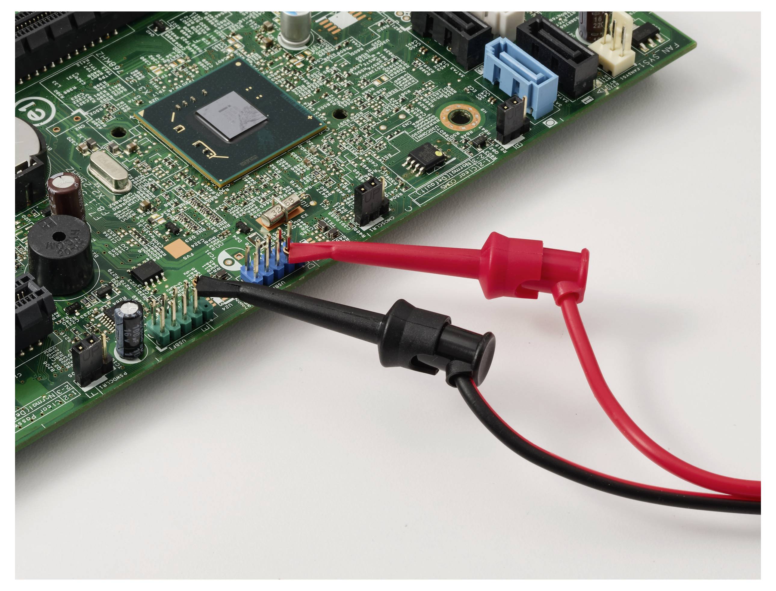 Eine elektronische Leiterplatte wird mit einem Multimeter getestet, wobei rote und schwarze Messspitzen an verschiedenen Punkten angeschlossen sind.
