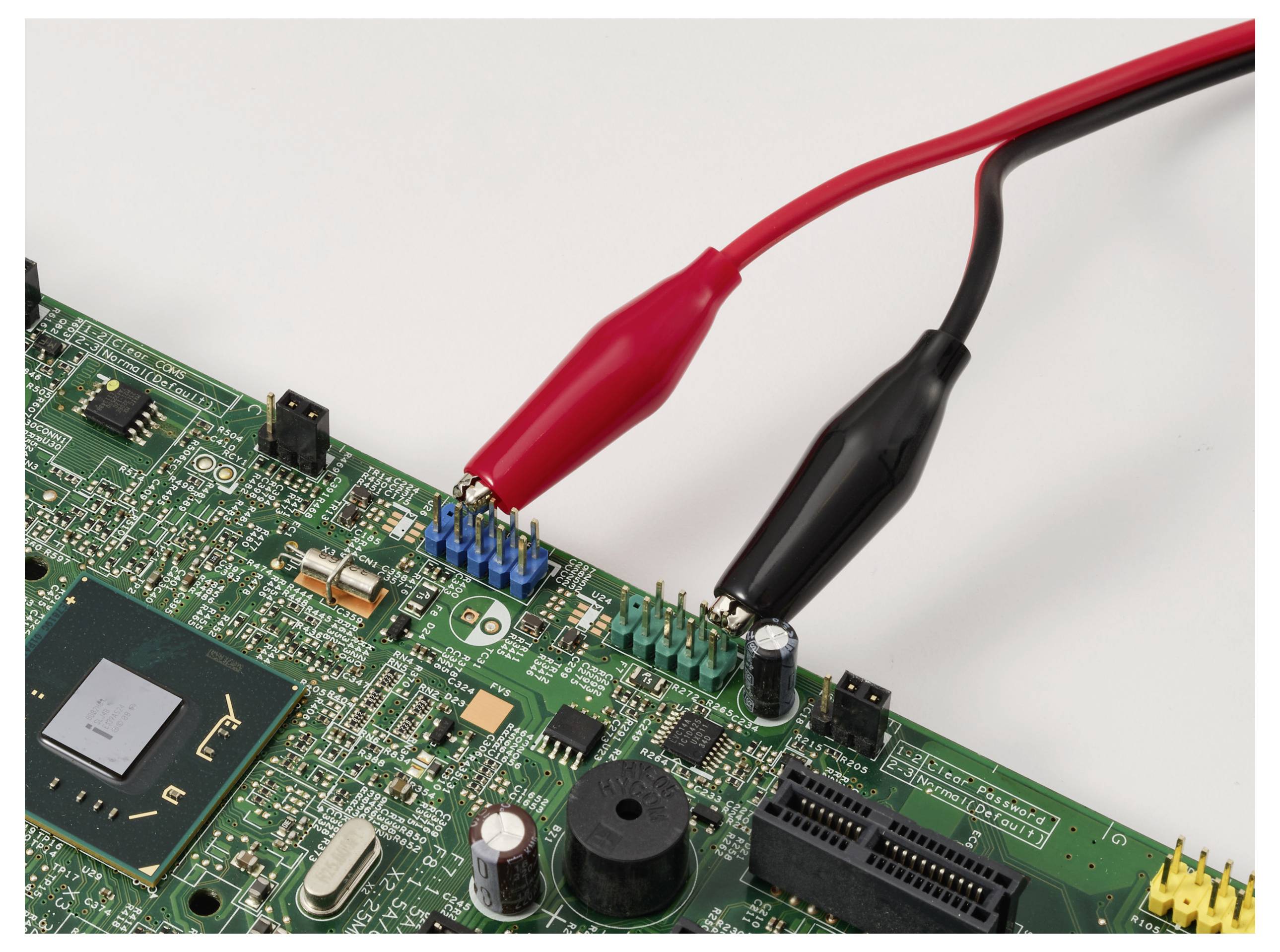 Eine Platine mit roten und schwarzen Krokodilklemmen, die eine elektrische Test- oder Reparatursituation anzeigen.