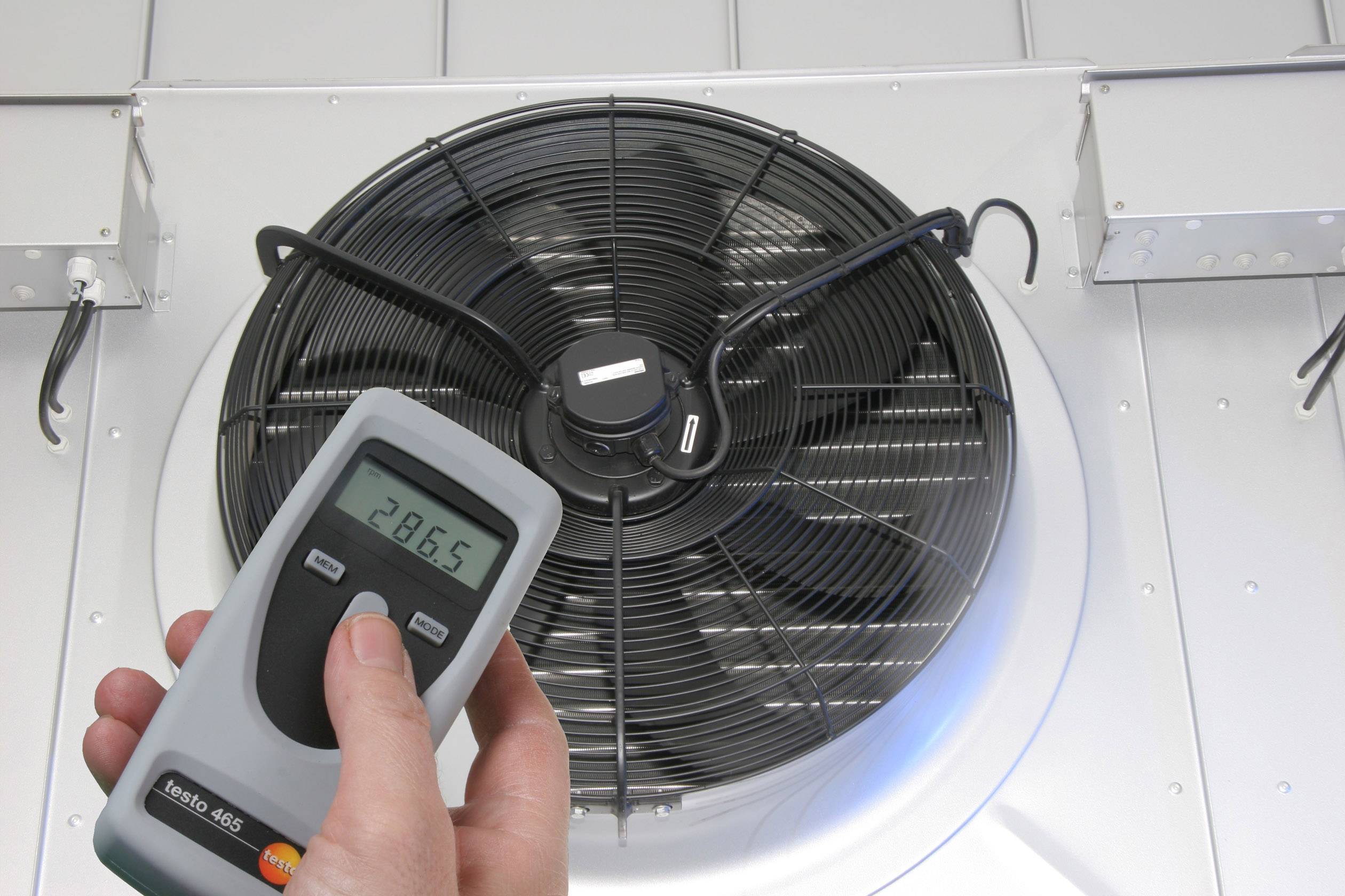 Ein Handgerät zeigt '28,65', gehalten vor einem großen Ventilator in einem Lüftungssystem. Indikator für Temperatur/Klimakontrolle.