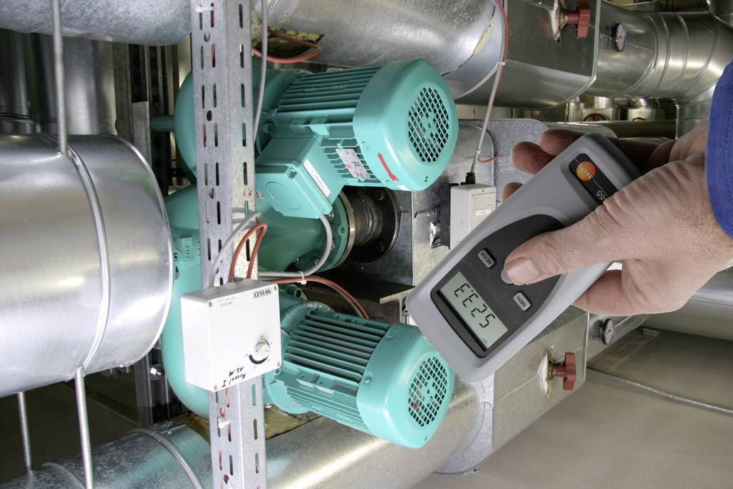 Eine Person misst mit einem digitalen Gerät die elektrische Leistung von zwei grünen Motoren in einer industriellen Anlage.