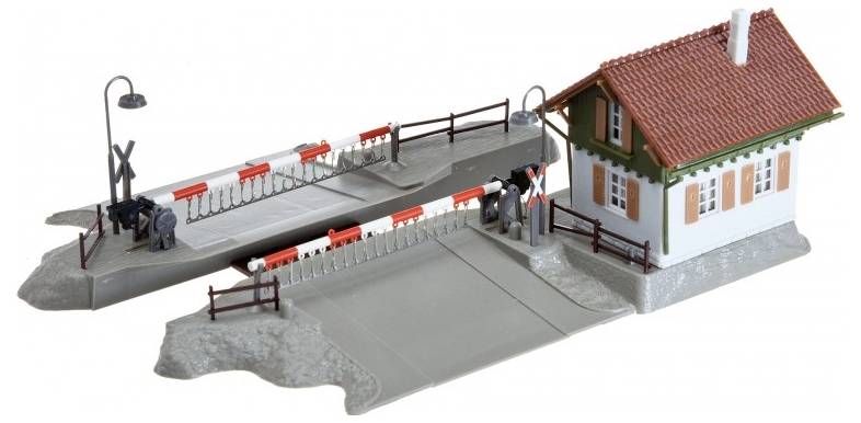 Eine Modelleisenbahnkreuzung mit Schranken und einem kleinen Gebäude, komplett mit detaillierten Merkmalen, einschließlich einer Laterne und einem Zaun.