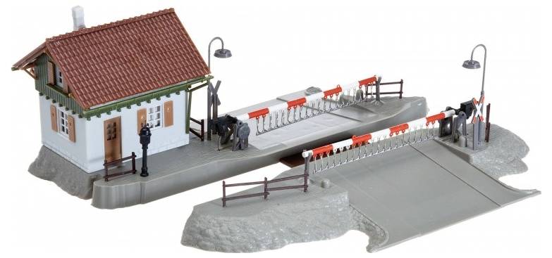 Modelleisenbahn-Bahnübergang mit einem Wachhaus, zwei rot-weißen Schranken und zwei schwarzen Spielfiguren, montiert auf einer grauen Basis mit Straßenlaternen.