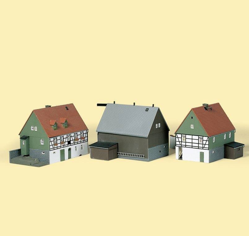 Drei Modellgebäude mit deutscher Architektur: zwei grüne Fachwerkhäuser mit roten Dächern und ein graues Industriegebäude.