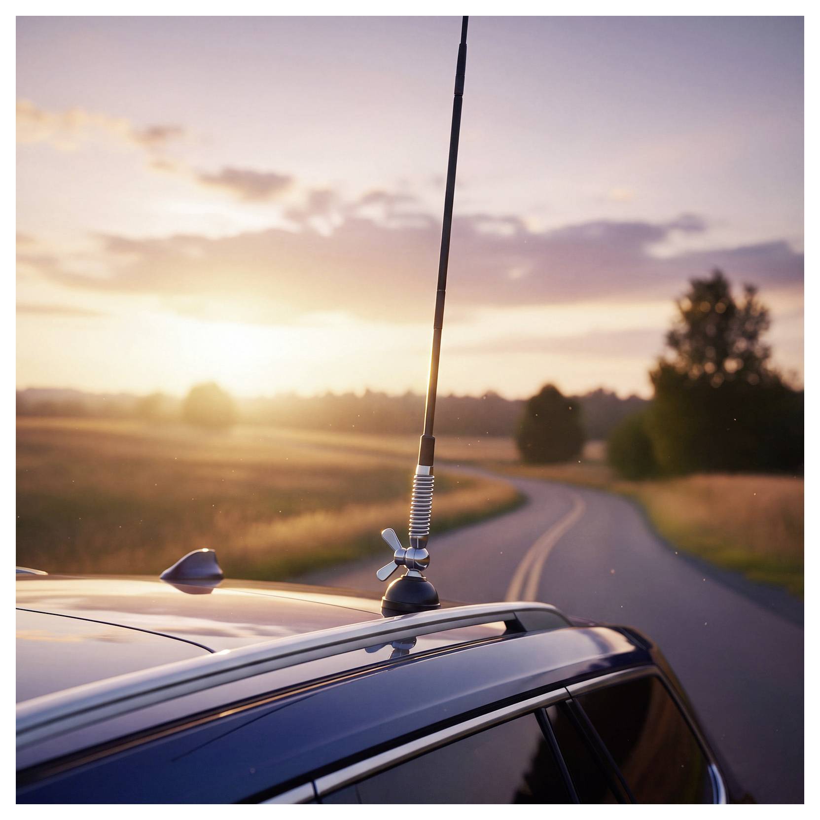 Autodach mit Antenne auf einer kurvenreichen Landstraße bei Sonnenuntergang, mit Feldern und Bäumen im Hintergrund.