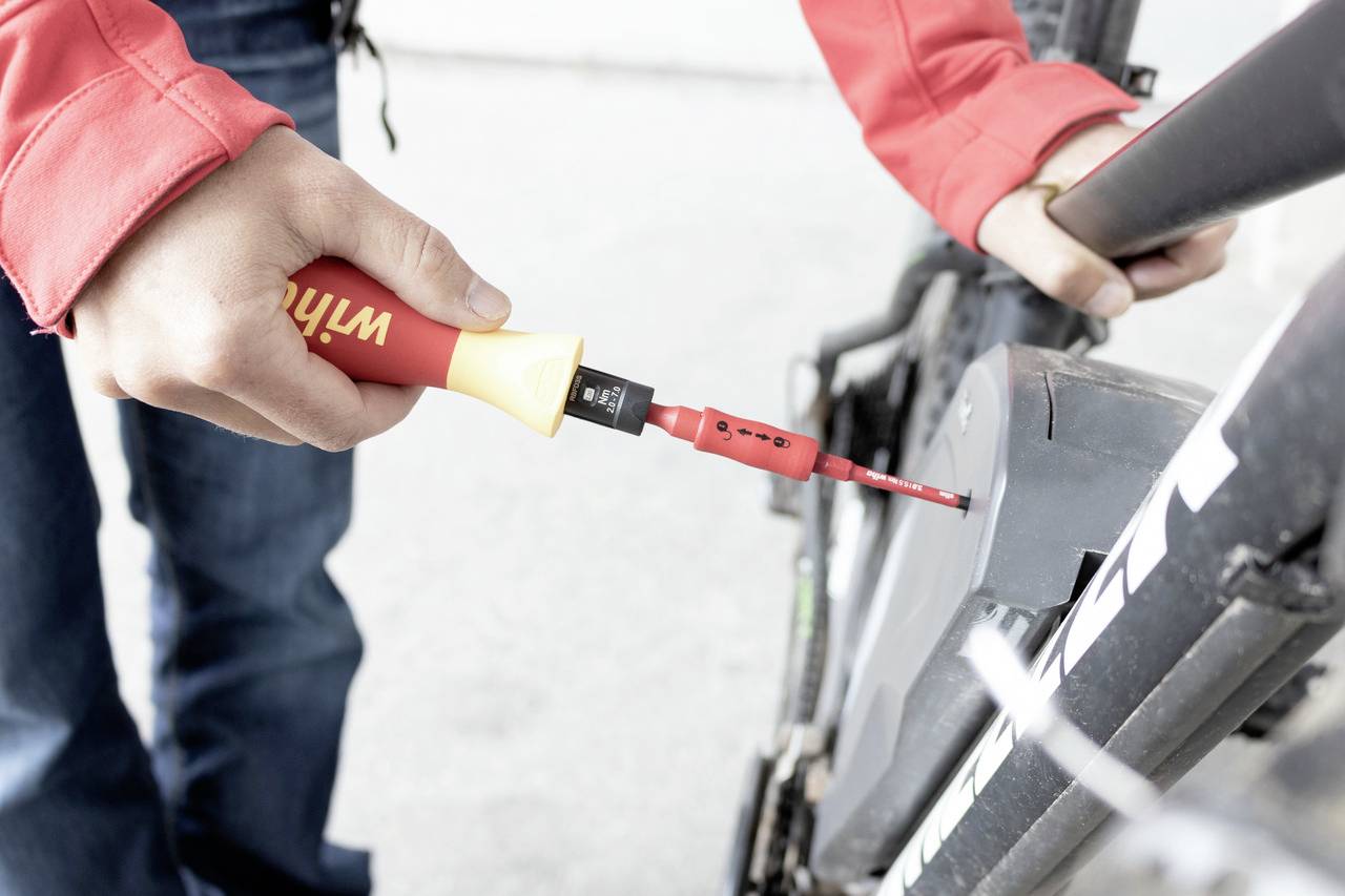 Eine Person repariert ein Fahrrad, indem sie mit einem Schraubendreher an einem Teil des Rahmens oder des Rads arbeitet.