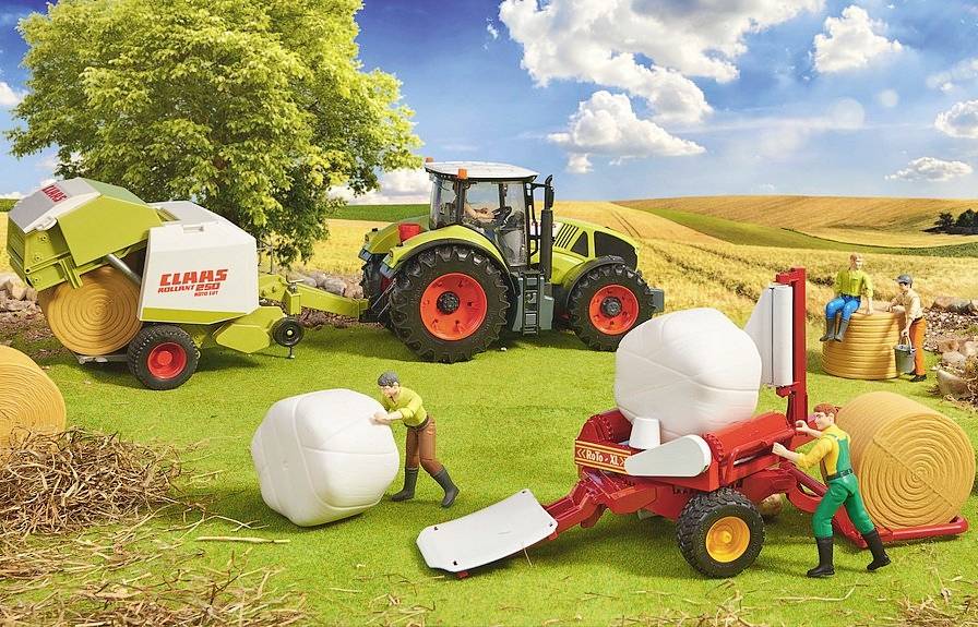 Ein Traktor mit Anhänger presst Heuballen auf einem Feld. Menschen rollen Heuballen. Ein sonniger Tag mit blauen Himmel und Wolken.