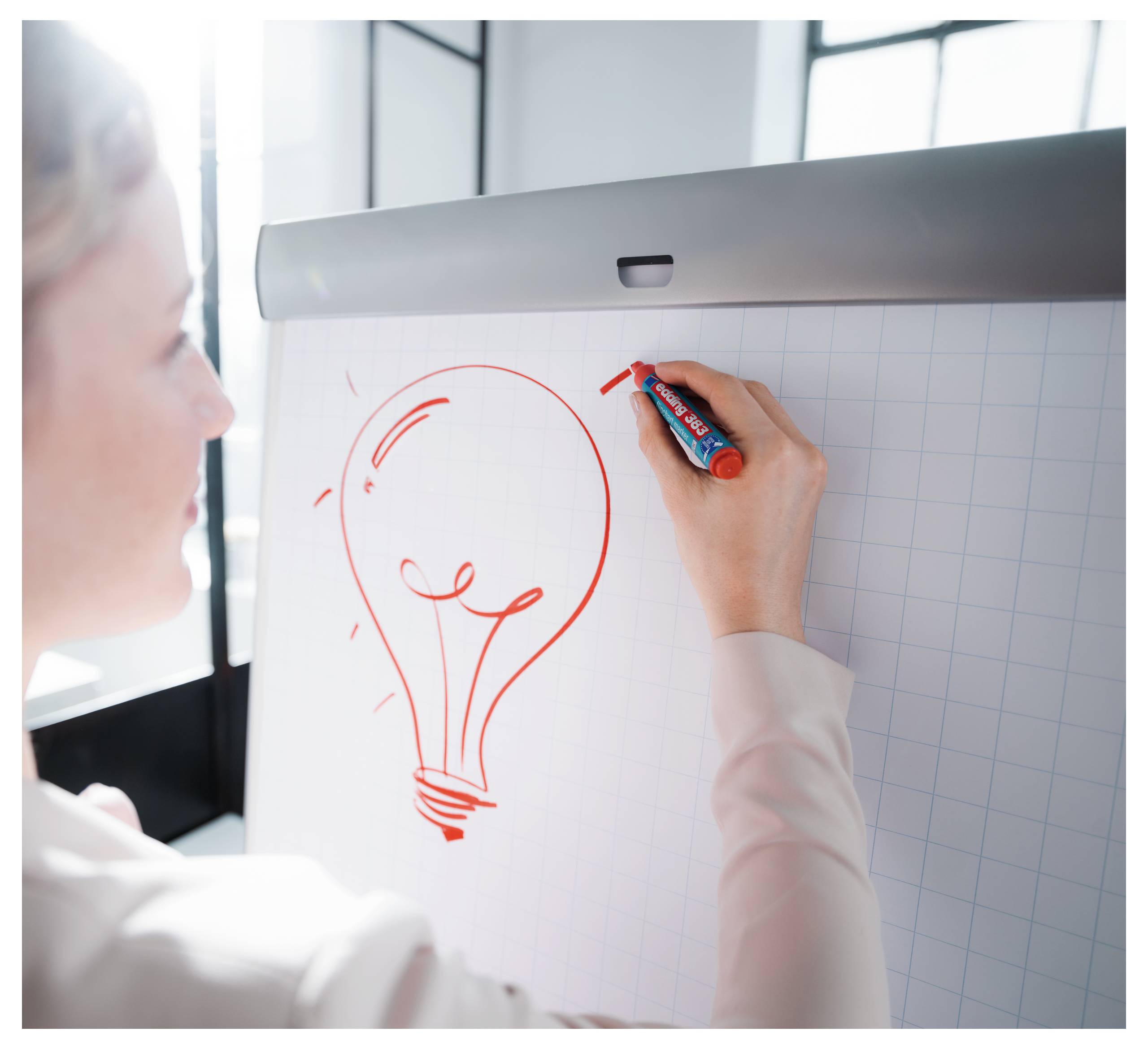 Person, die ein Glühbirnensymbol auf einem Flipchart zeichnet und Brainstorming oder eine neue Idee andeutet.