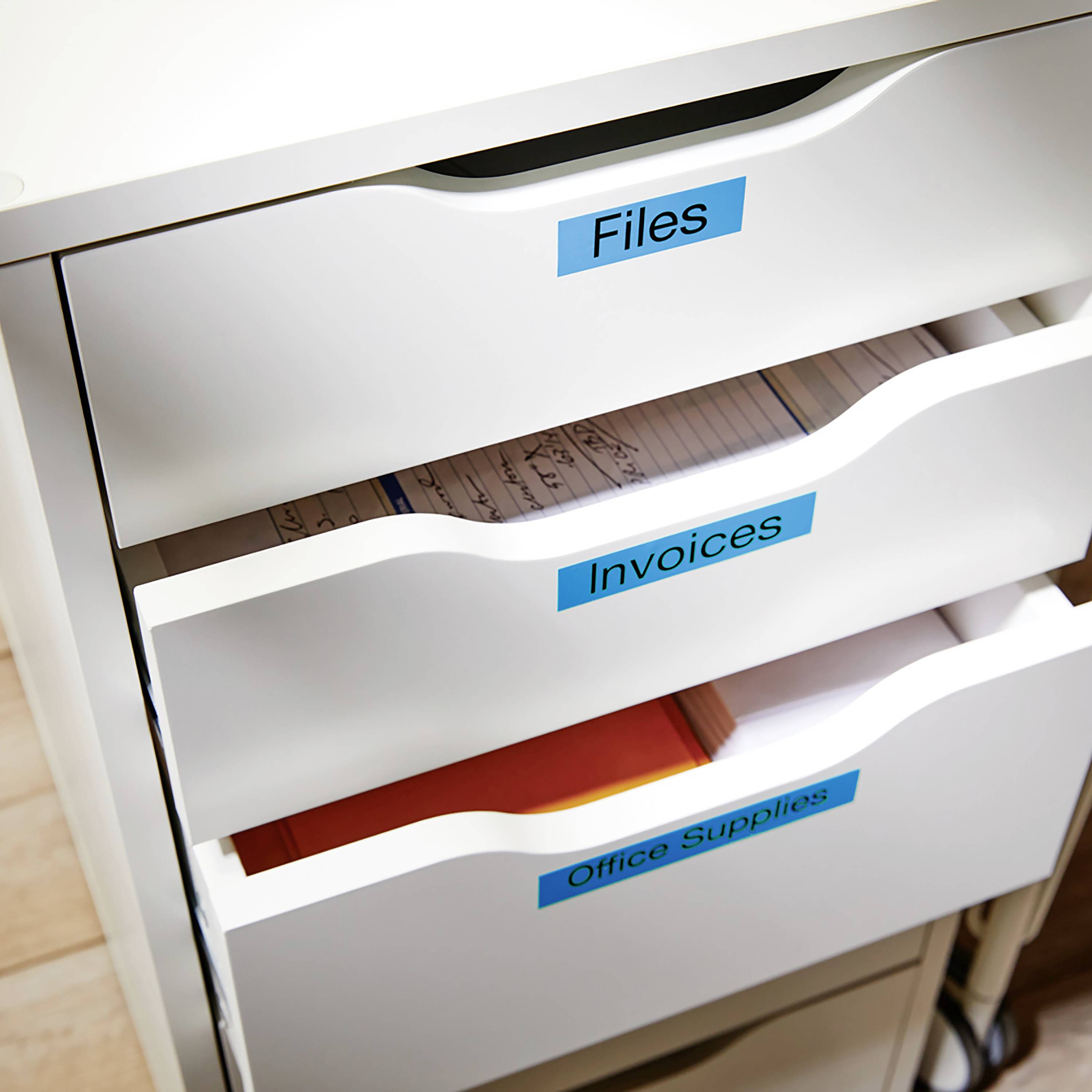 Ein weißer Schrank mit drei offenen Schubladen, beschriftet mit 'Files', 'Invoices' und 'Office Supplies', gefüllt mit Dokumenten und Büromaterial.