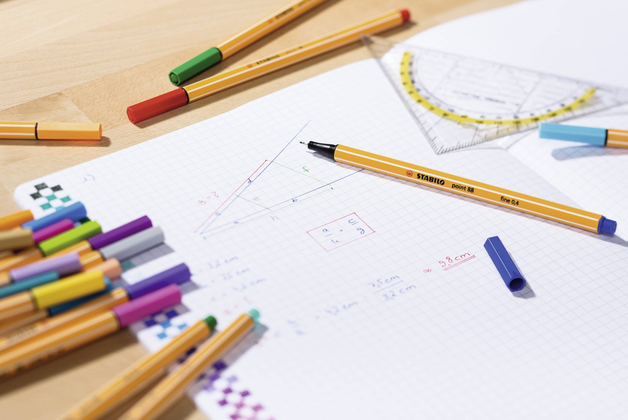 Mathe-Arbeitsblatt mit geometrischen Zeichnungen, bunten Stiften und einem Geodreieck. Hauptfokus auf einem gezeichneten Dreieck.