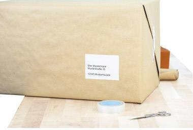 Ein verpacktes Paket auf einem Tisch mit einer Adresse darauf. Daneben liegen Klebeband und Schere.