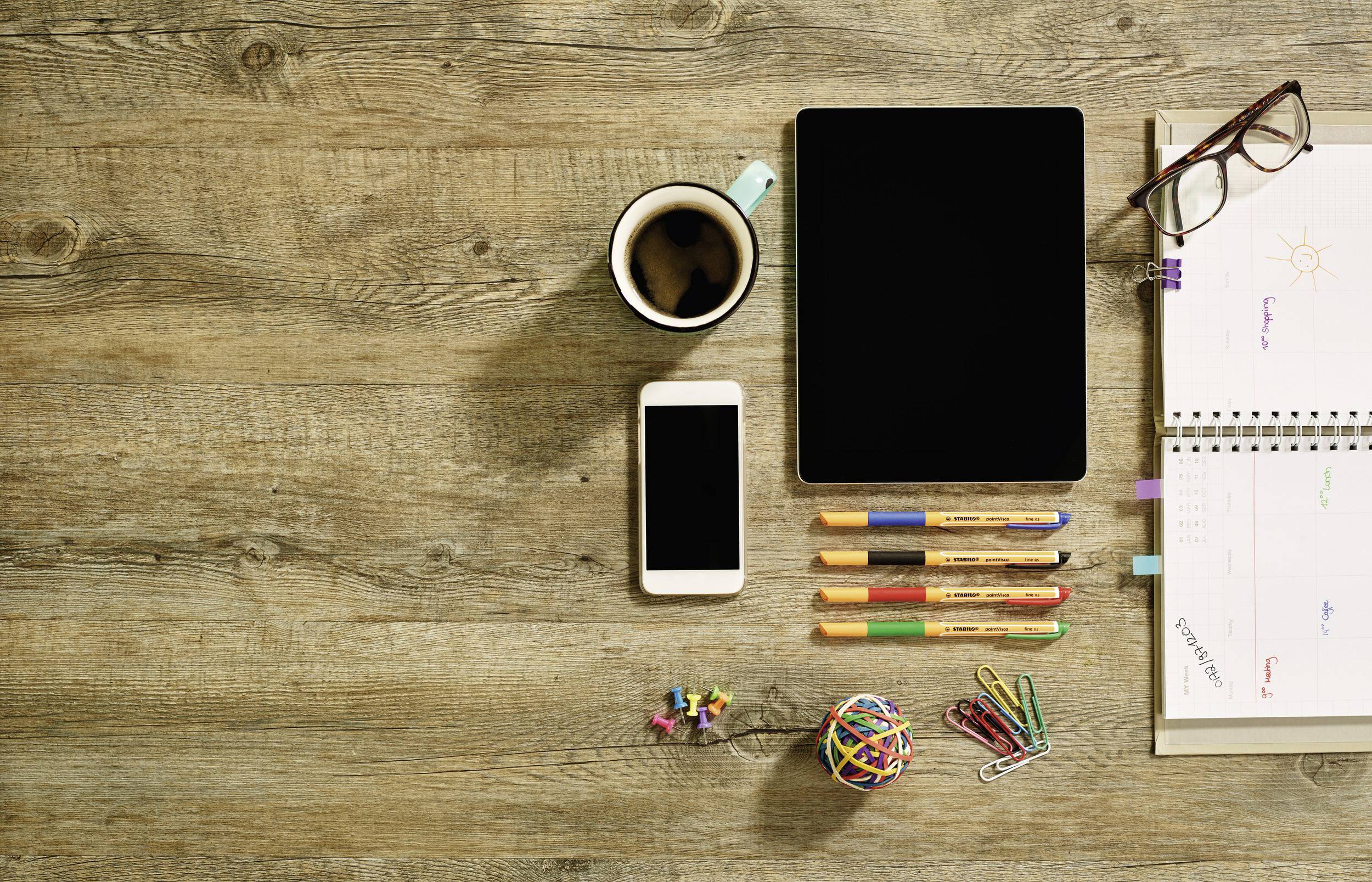 Tablet, Smartphone, Kaffee, Stifte, Notizbuch auf Holz. Arbeitsplatz mit digitalen und analogen Tools, bereit für kreative Arbeit oder Planung.
