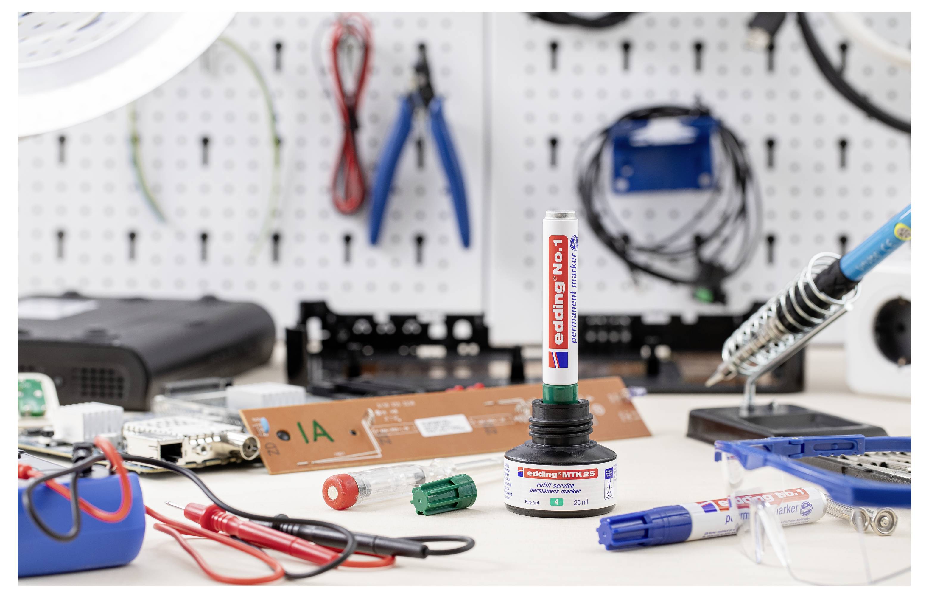 Elektronische Werkbank mit einem Lötkolben und Werkzeugen, zentriert auf einem „Codier-Stift" in einem Halter, mit Leiterplatten, Drähten und Komponenten, die auf dem Tisch verteilt sind.