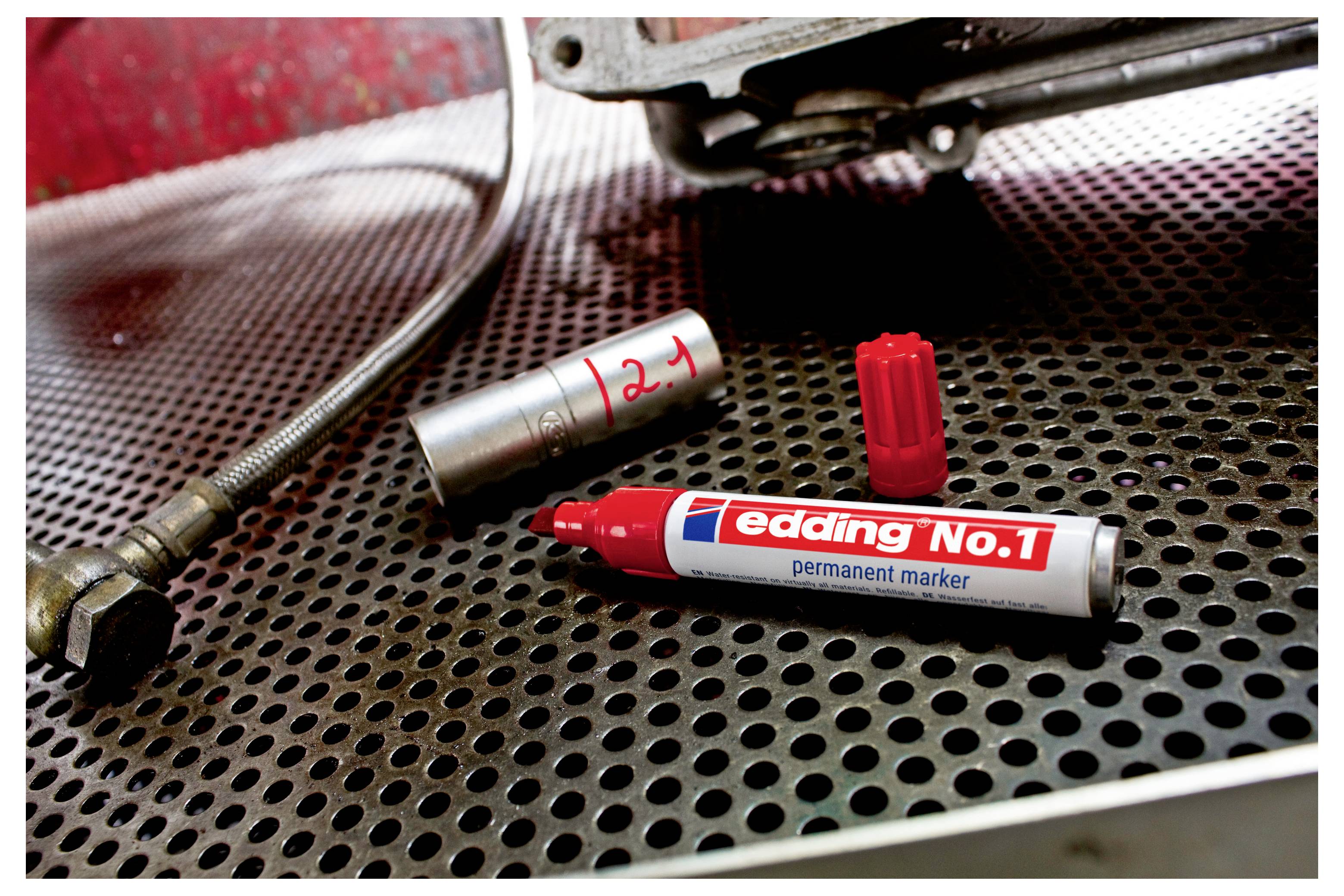 Zwei rot gespitzte Permanentmarker und ein silberner Marker mit rotem „2-1" auf einer perforierten Metall-Werkbank neben einem Schlauch und Maschinen.