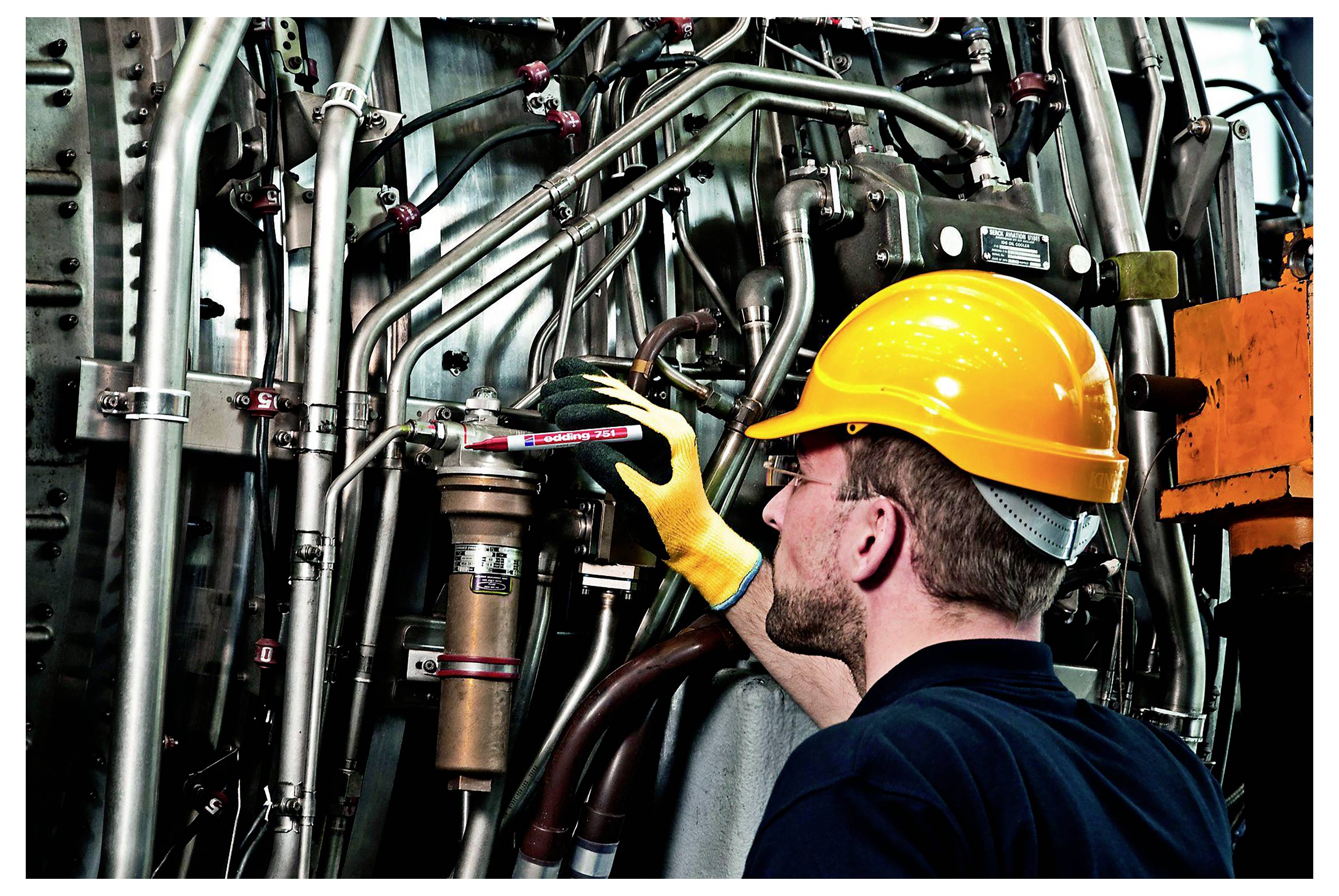Arbeiter in einem gelben Schutzhelm inspiziert Industrierohre und Maschinen in einer Fabrik.