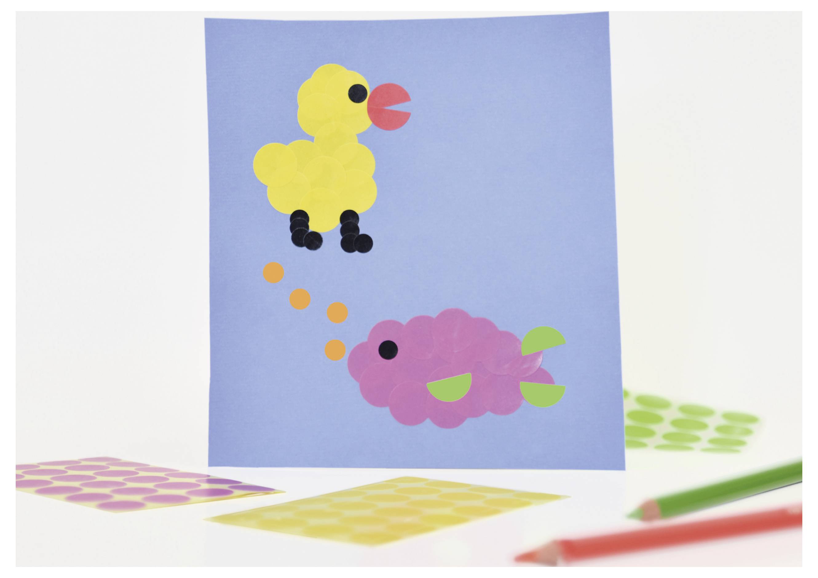 Bastelbild mit gelbem Vogel oben und rosa Fisch unten auf blauem Hintergrund; bunte Papierformen liegen drumherum.