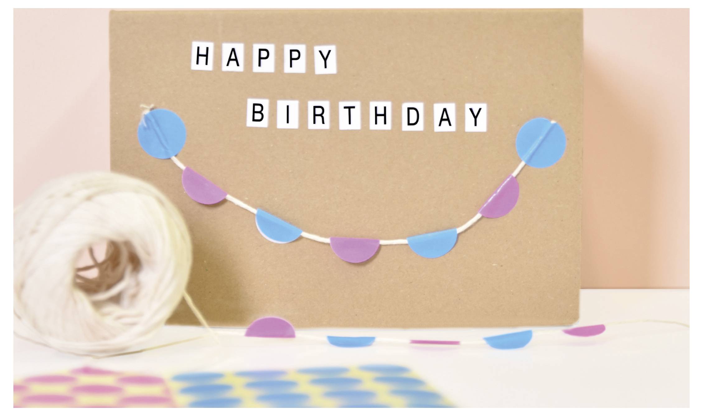 Geburtstagskarte mit der Aufschrift 'HAPPY BIRTHDAY', dekoriert mit farbiger Girlande und Pastellbällen.