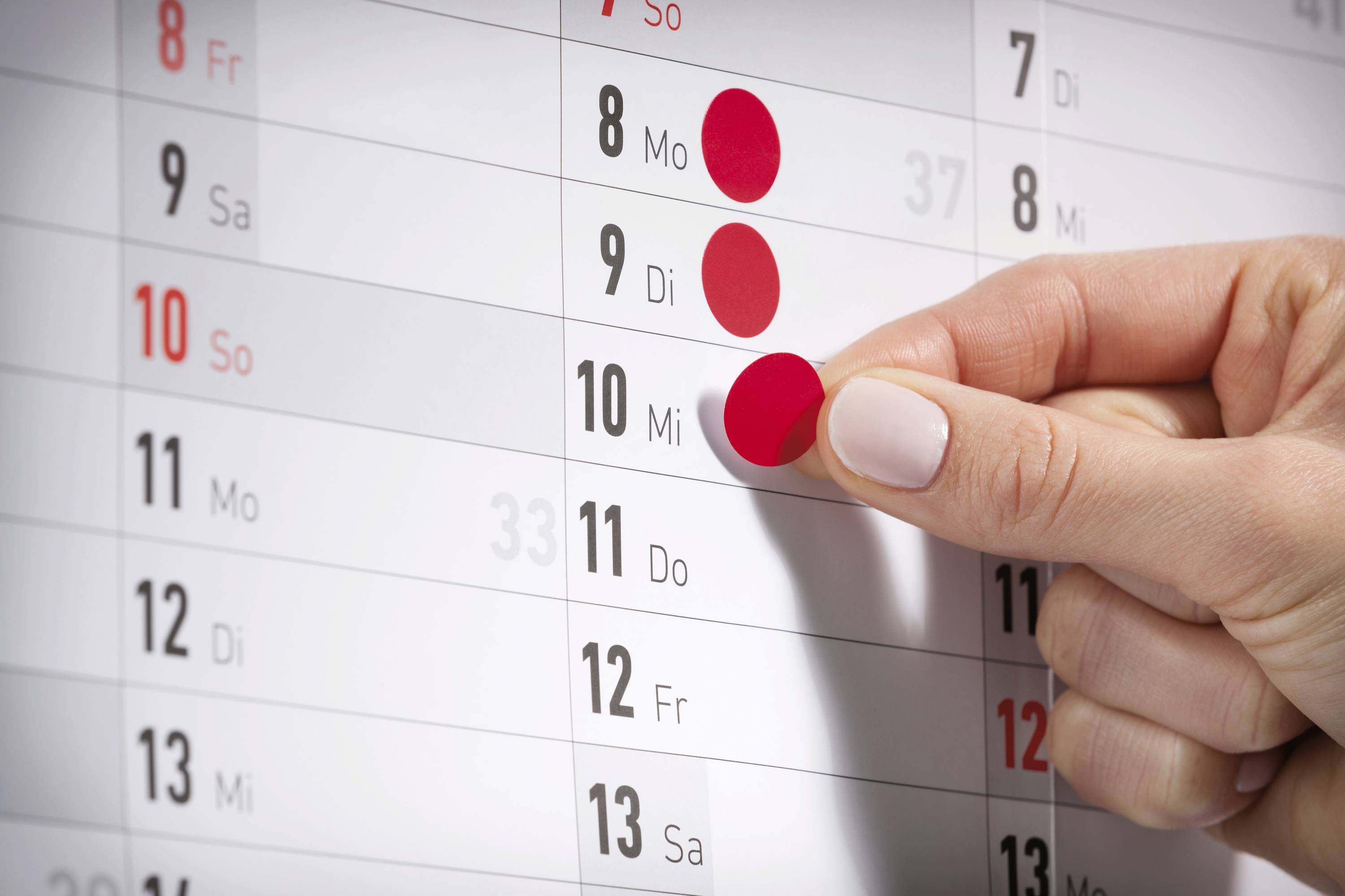 Eine Hand markiert den 10. März auf einem Wandkalender mit einem roten Punkt.