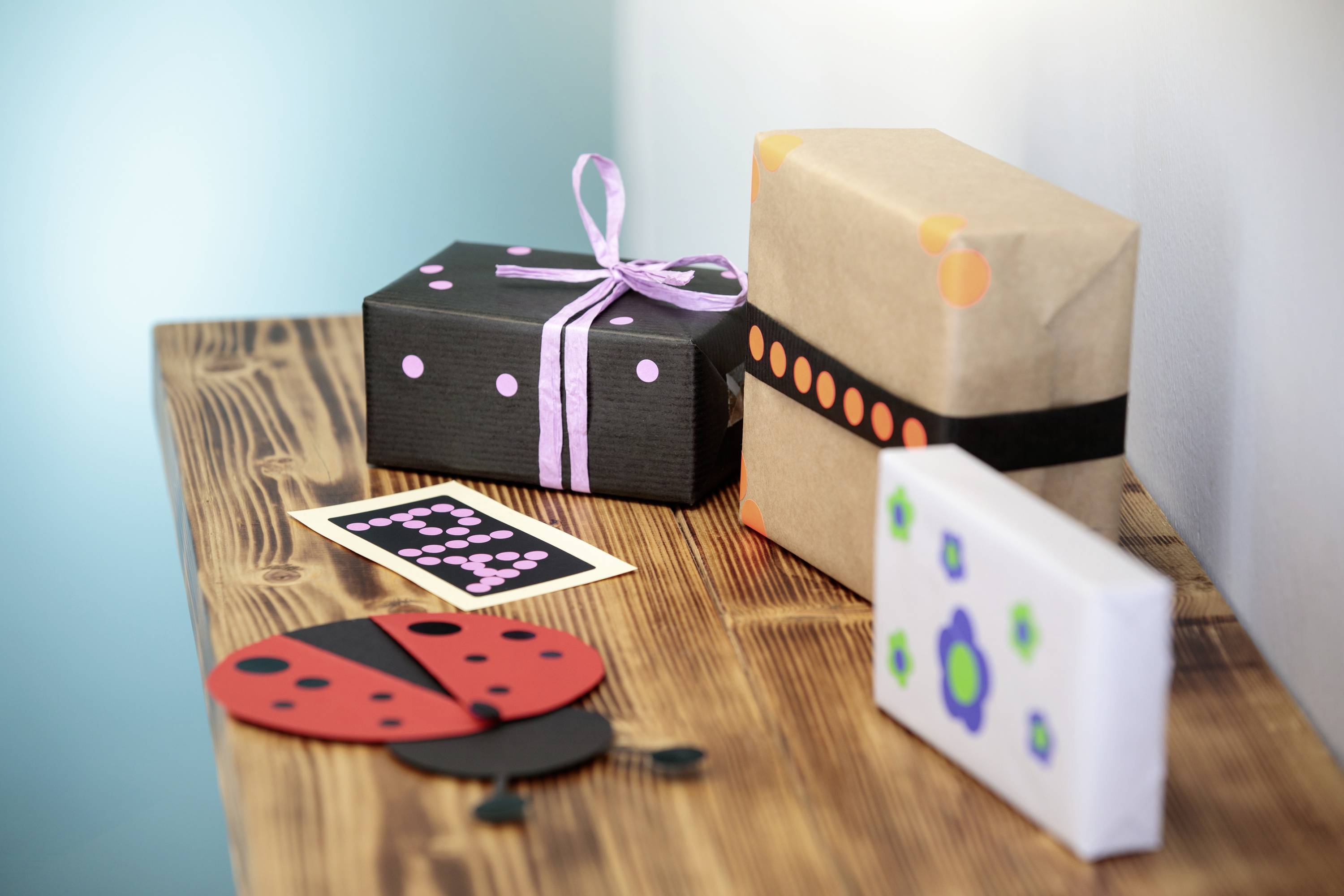 Mehrere bunt verpackte Geschenke und eine Karte auf einem Holztisch. Ein Geschenk ist mit pinkem Band verziert.