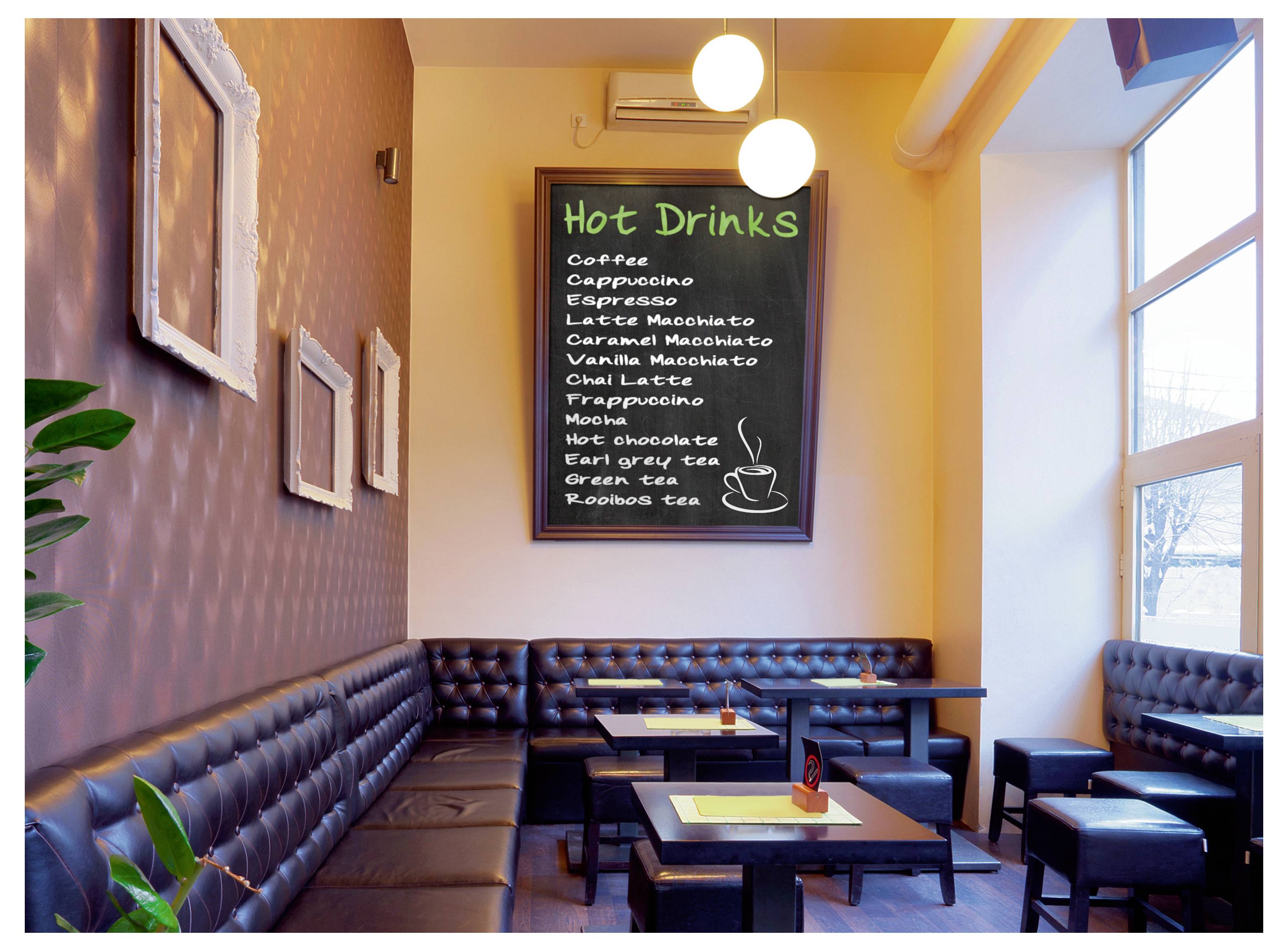 Gemütlicher Sitzbereich in einem Café mit schwarzen Lederbänken und Tischen unter einem Wandmenü mit der Aufschrift "Heißgetränke", auf dem Kaffee-, Tee- und Schokoladenoptionen aufgelistet sind.