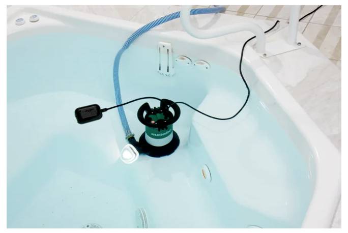 Eine Person mit Maske und Schutzausrüstung steht auf einer Plattform und installiert oder repariert eine Deckenleuchte in einer Industrieumgebung.