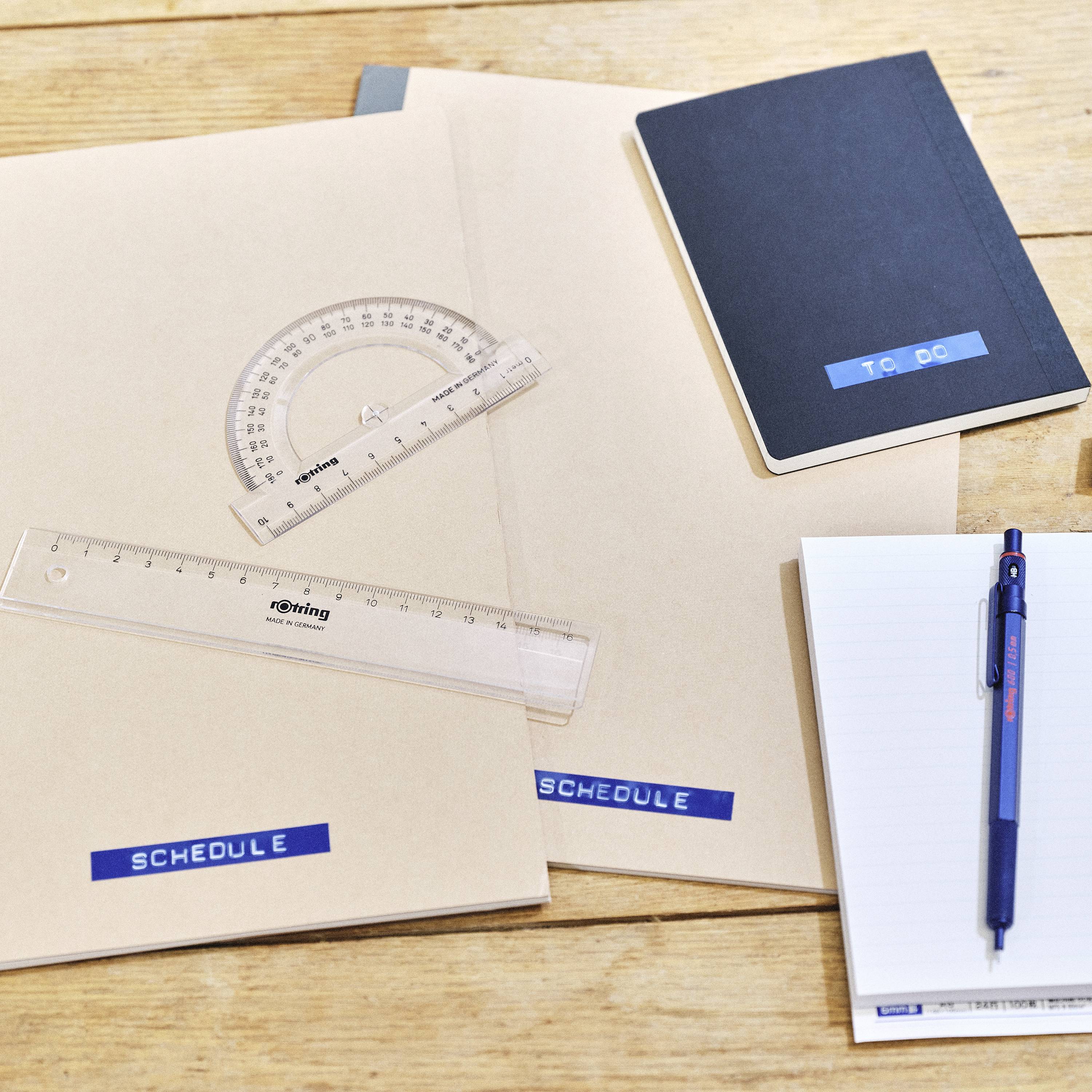 Ordnungsmaterialien auf einem Tisch: Notizbuch mit 'TO DO', ein Lineal, ein Winkelmesser, ein Planer mit 'SCHEDULE', Stift auf Notizblock.