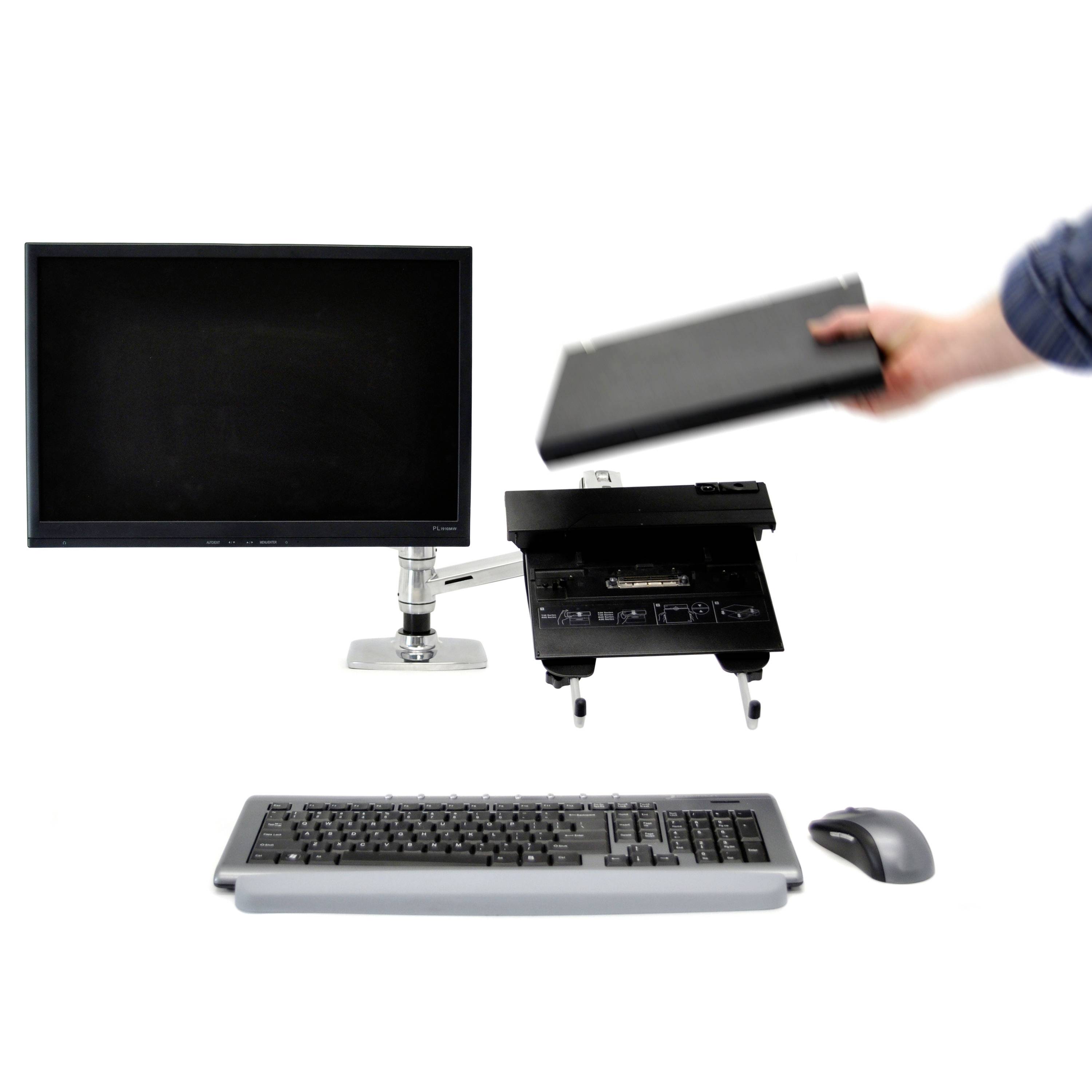Ein Arbeitsplatz mit Monitor, Tastatur und Maus. Eine Person hält einen geschlossenen Laptop.