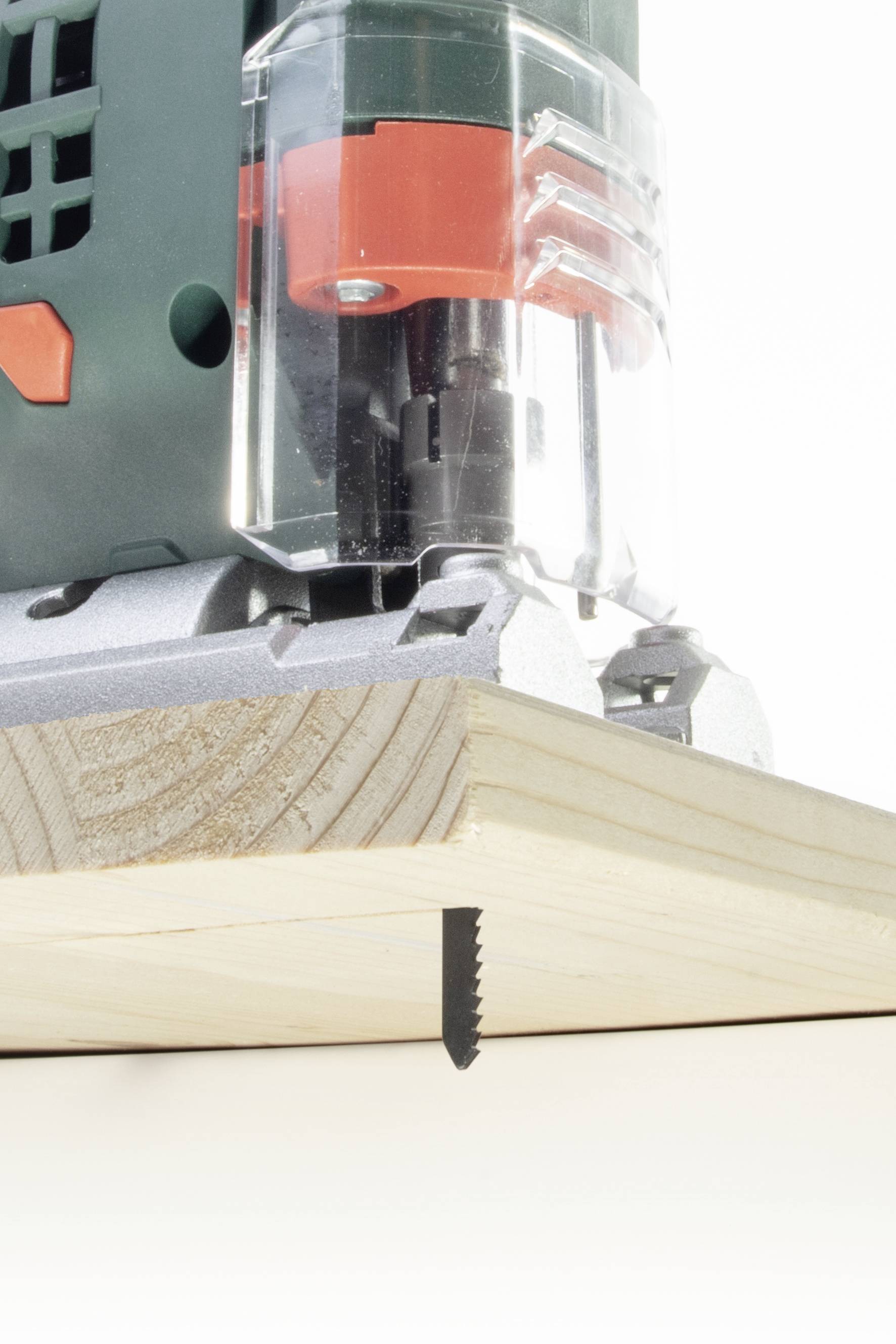 Eine grüne Stichsäge mit rotem Detail schneidet Holz in einer Schräge. Das Sägeblatt ist teilweise sichtbar unter dem Werkstück.