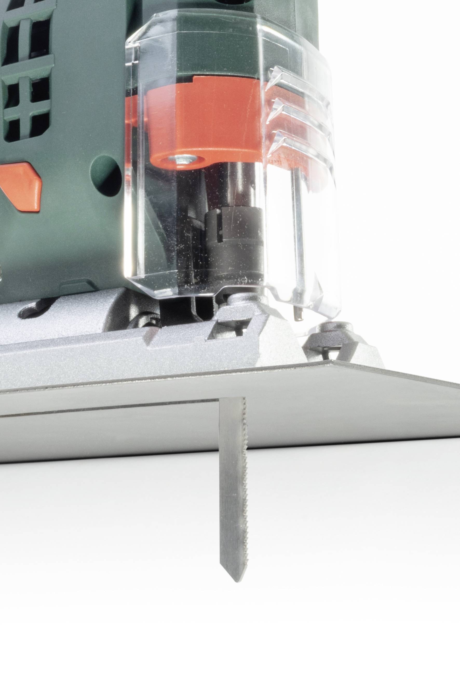 Eine grüne Stichsäge mit durchsichtigem Schutz und rot-schwarzem Detail schneidet durch ein graues Holzstück.