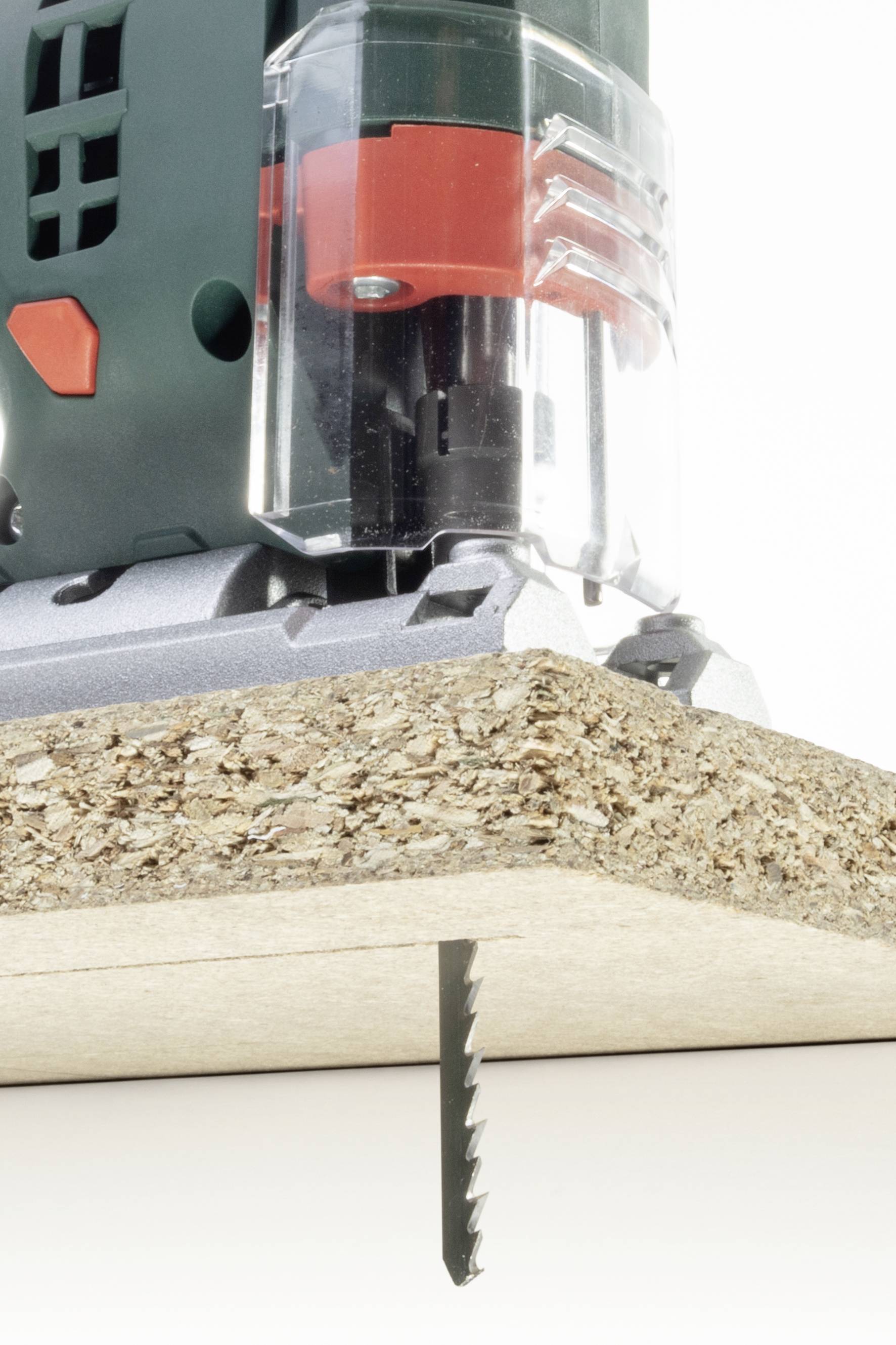 Elektrische Stichsäge schneidet eine Spanplatte. Nahaufnahme des Sägeblatts, das von unten nach oben durch das Material arbeitet.