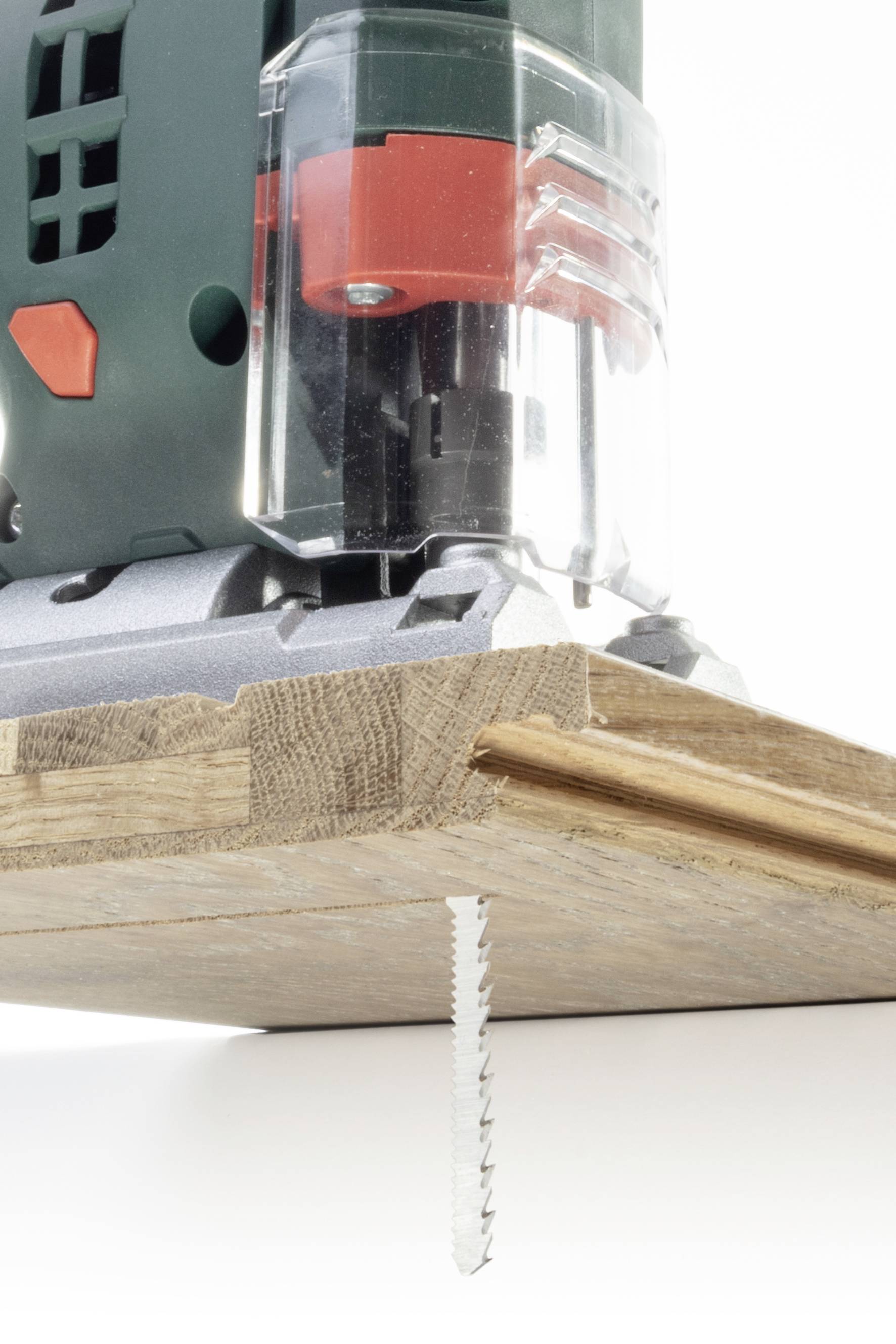 Ein elektrischer Stichsägenkopf schneidet präzise durch ein Holzbrett. Links Grün und Schwarz, vorne ein gezacktes Sägeblatt.