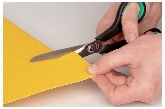 Hände, die mit einer Schere ein Stück gelben Wellpappe ausschneiden und dabei eine Bastel- oder Kunstaktivität demonstrieren.