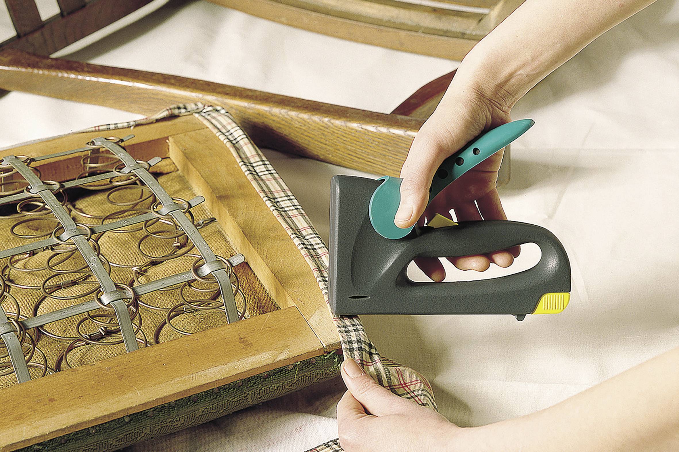 Person polstert einen Stuhlrahmen mit einem Handtacker und befestigt Stoff an der Sitzfläche.