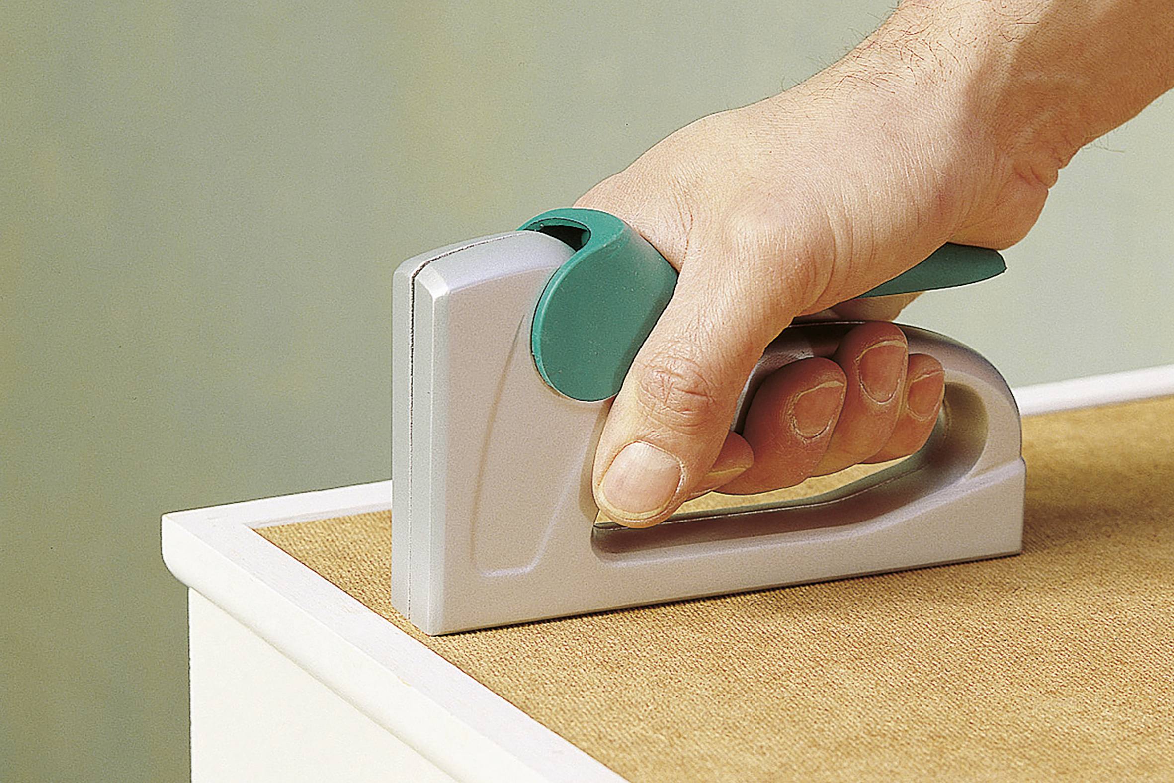 Eine Hand hält einen Tacker, der an einer Kante eines Holzstücks eingesetzt wird, um es zu befestigen oder zu fixieren.