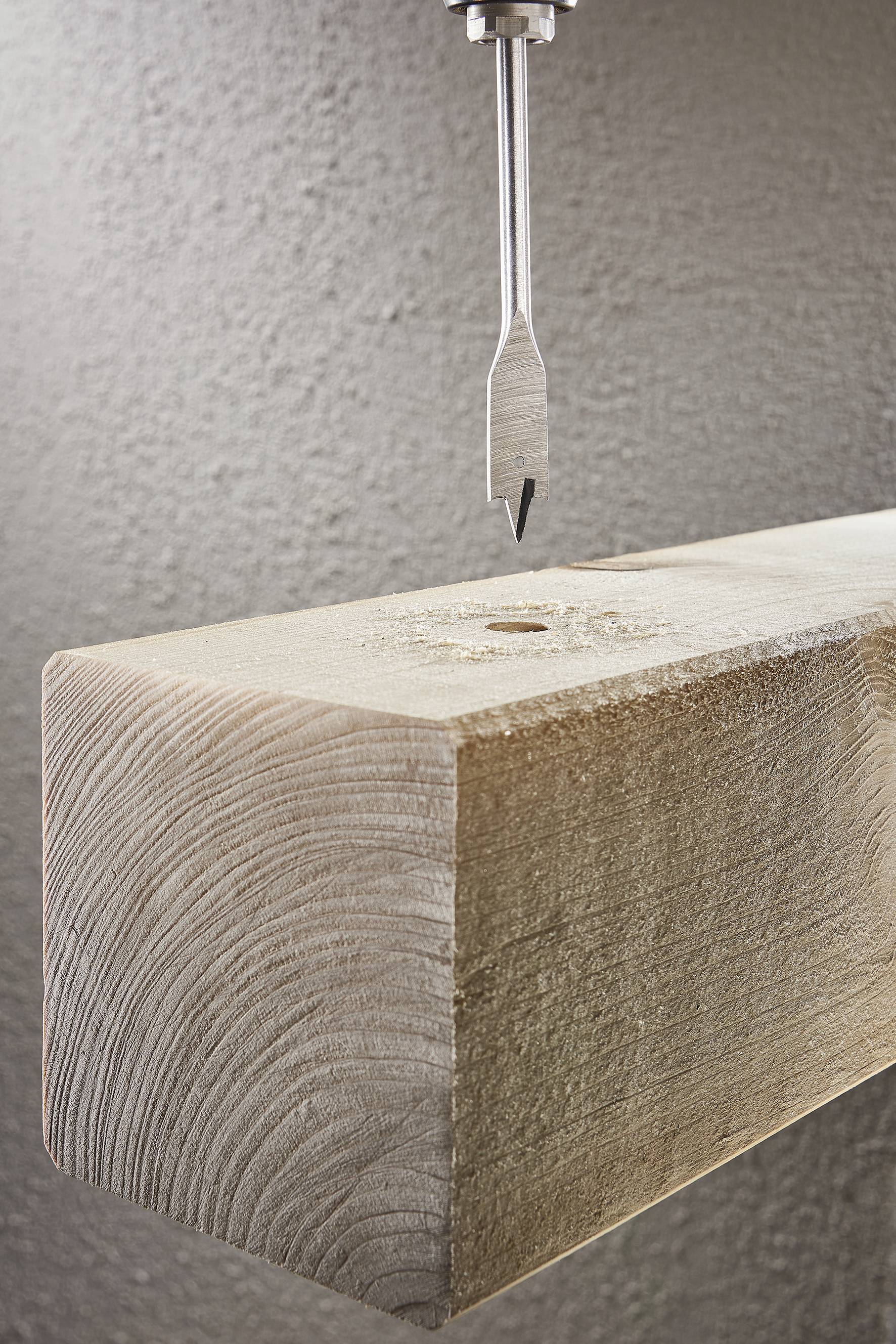 Ein Holzbohrer nähert sich einem Holzblock von oben, bereit, ein Loch in das Holz zu bohren.