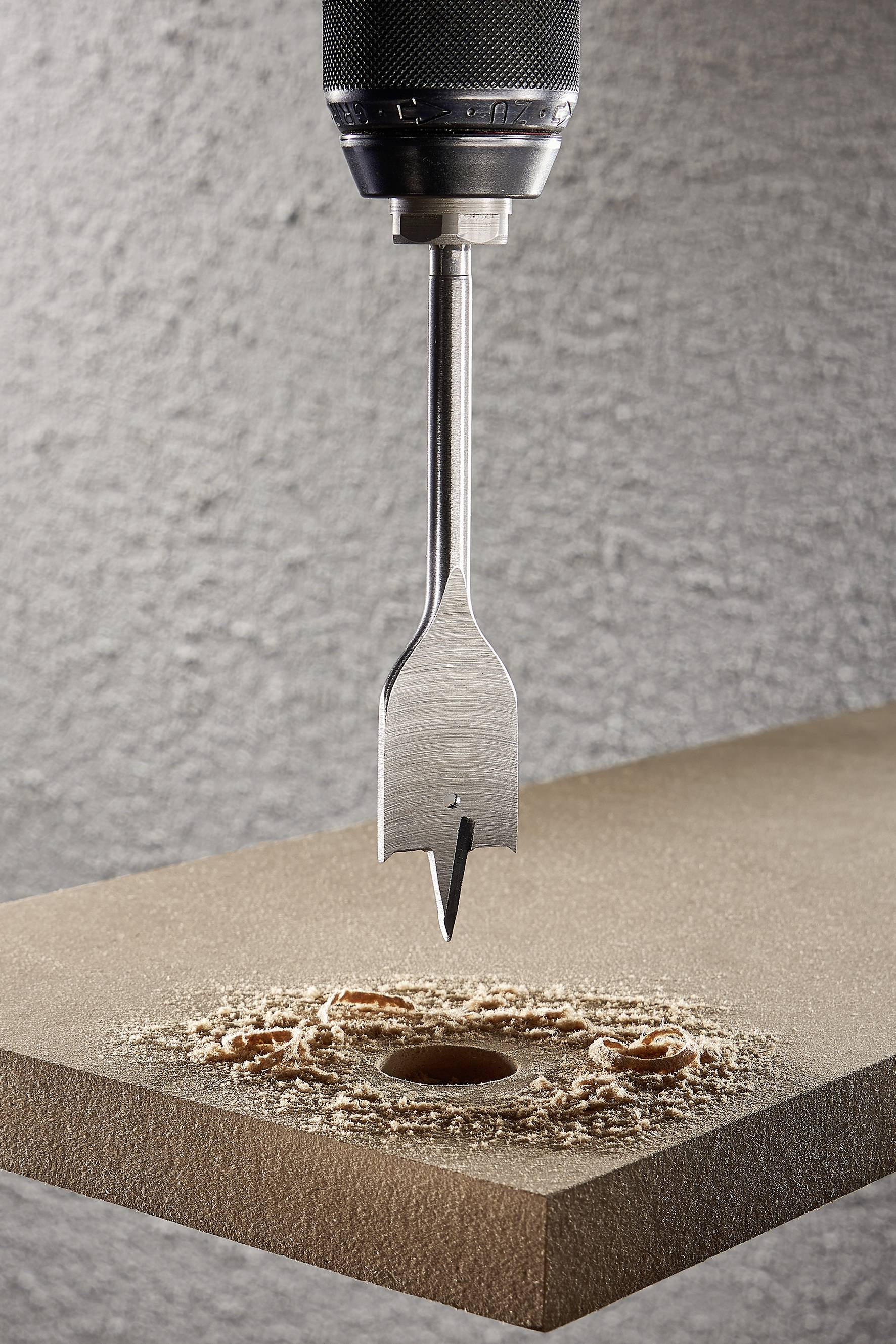 Ein Bohrer dringt durch ein Holzbrett, erzeugt ein präzises Loch, umgeben von Sägespänen.