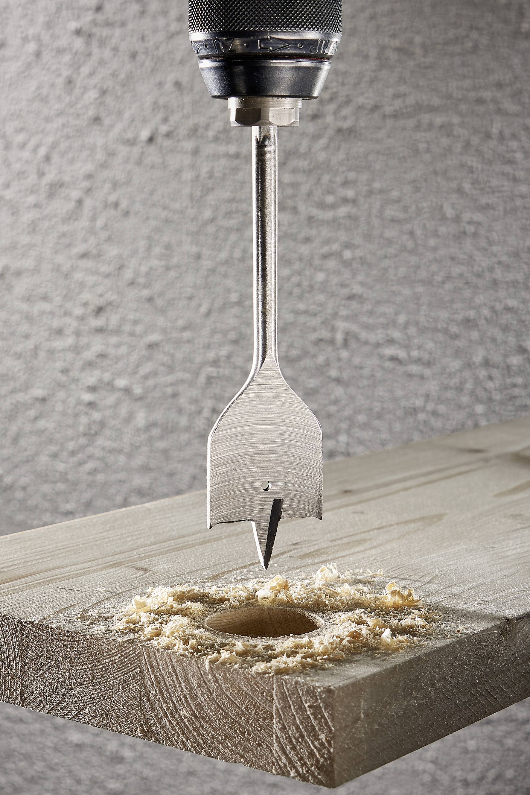 Ein Bohrer bohrt ein rundes Loch in ein Holzbrett, umgeben von Holzspänen.