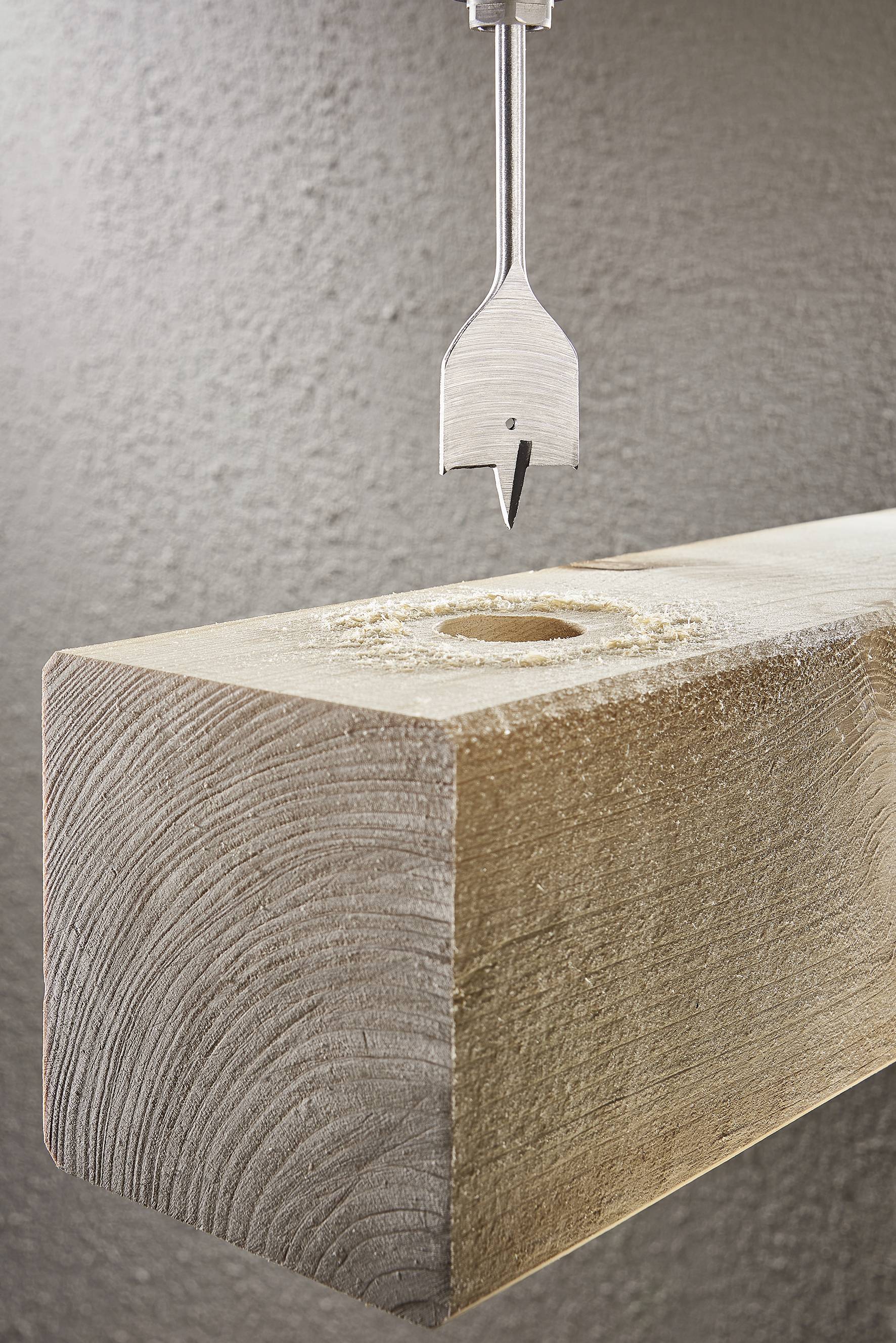 Ein Spiralbohrer schwebt über einem Holzbalken mit einem gebohrten Loch. Der Hintergrund ist strukturiert.