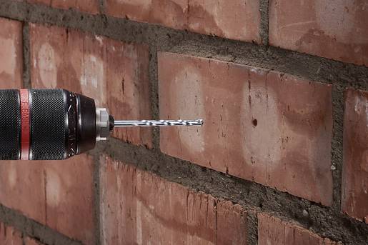 Eine Bohrmaschine bohrt ein Loch in eine Ziegelmauer. Der Bohrer ist auf die rechte Seite der Ziegel gerichtet.