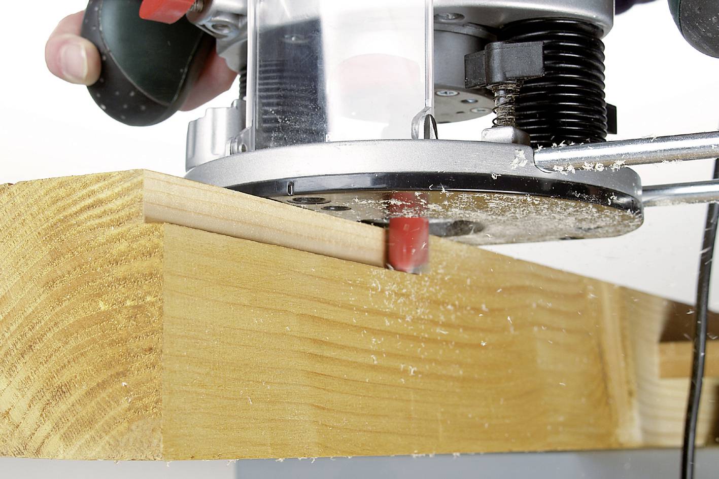 Eine Handfräse bearbeitet die Kante eines Holzstücks, erzeugt eine glatte Oberfläche und produziert Holzspäne.