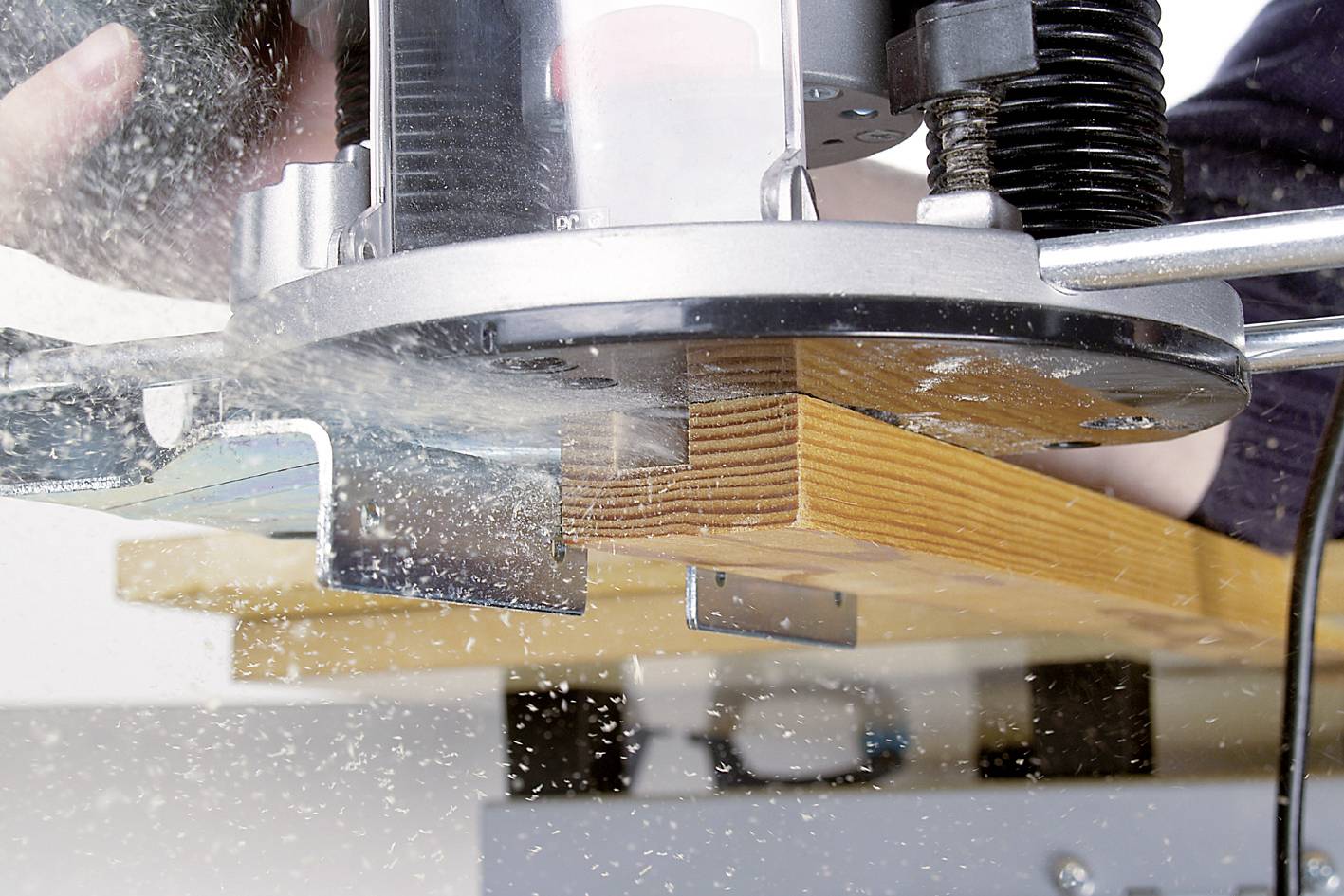 Eine Oberfräse bearbeitet ein Stück Holz. Holzspäne fliegen in die Luft. Das Gerät wird von einer Person bedient, Fokus auf die Maschine.