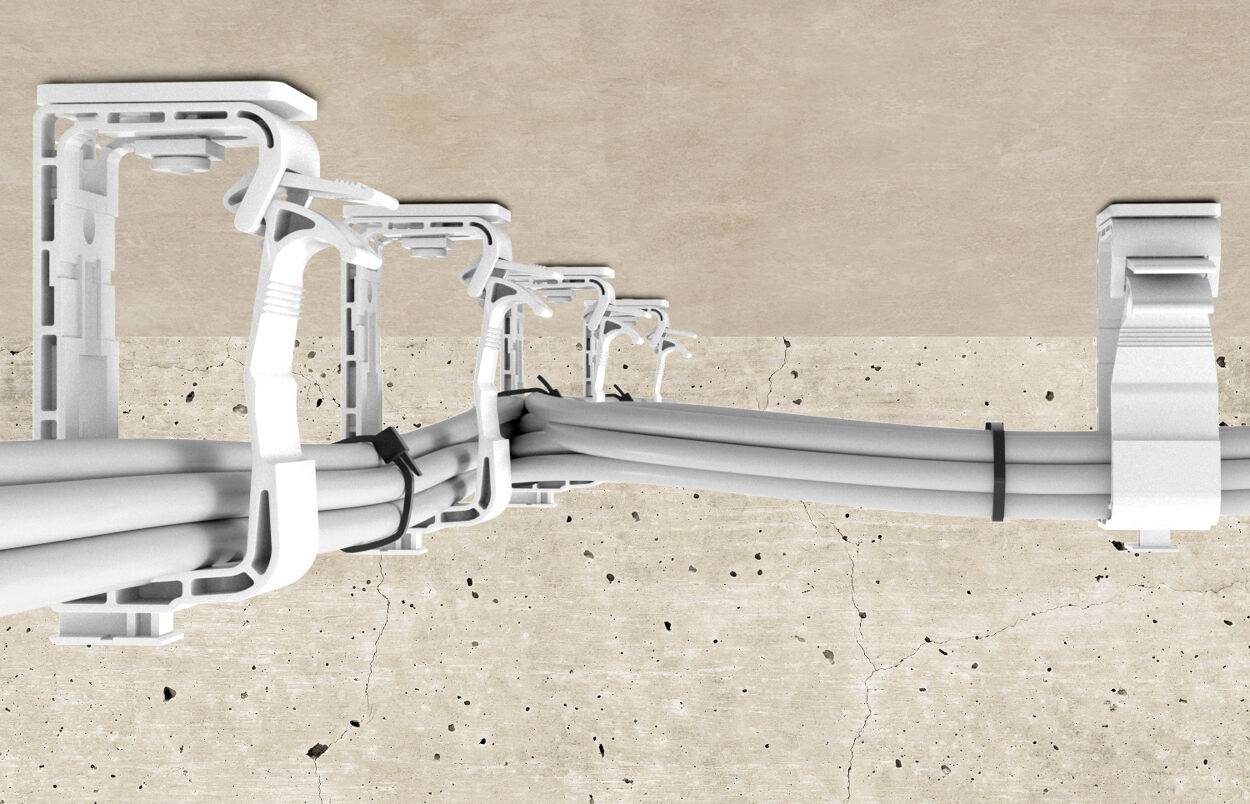 Kabelverlegung an einer Betonwand mit Kabelbindern und weißen Halterungen, die Stabilität und Ordnung gewährleisten.