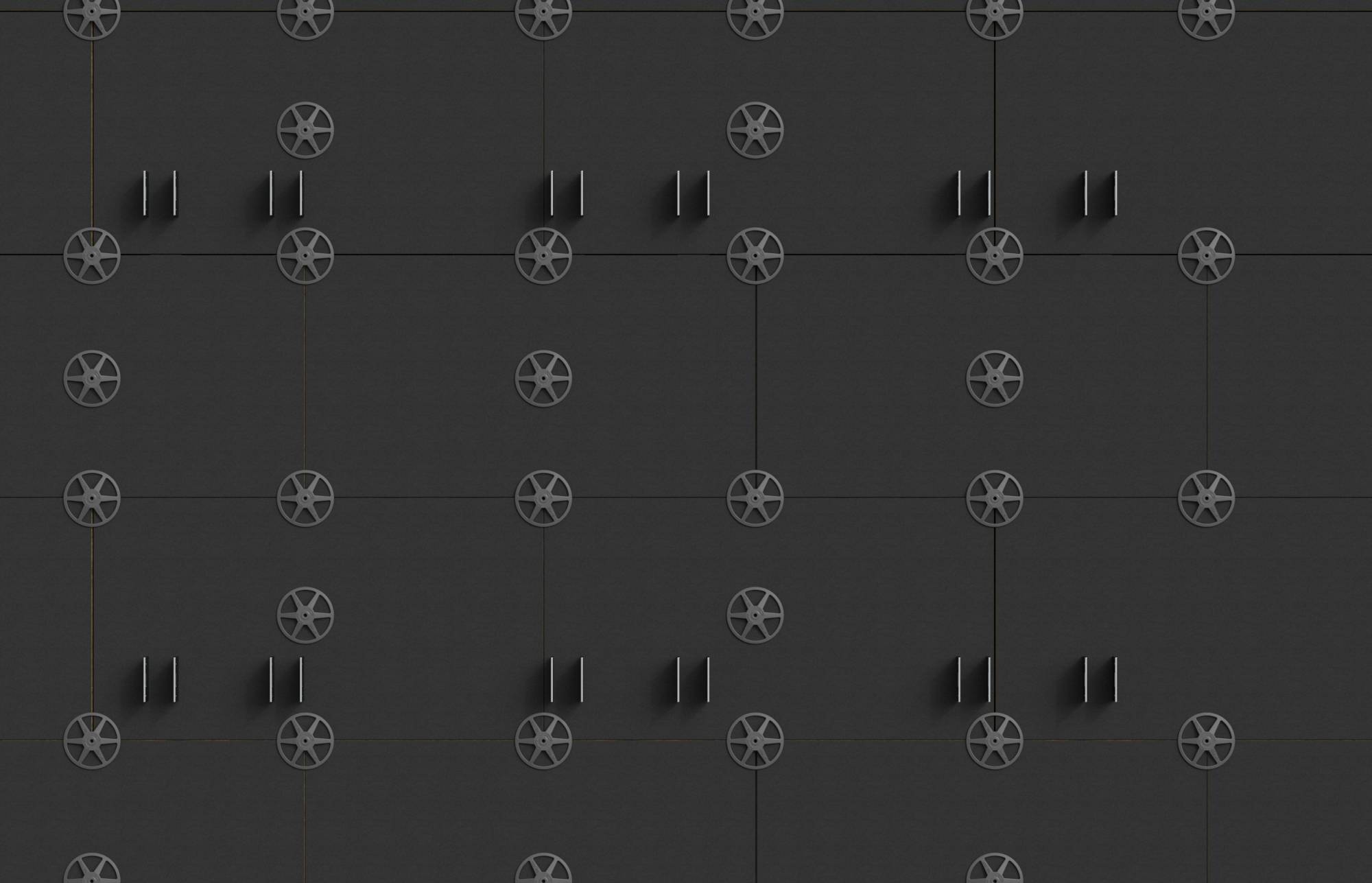 Dunkle Wand aus quadratischen Paneelen mit wiederholten kreisförmigen radähnlichen Emblemen und Paaren von kurzen vertikalen Griffen, die ein geometrisches Industriemuster erzeugen.