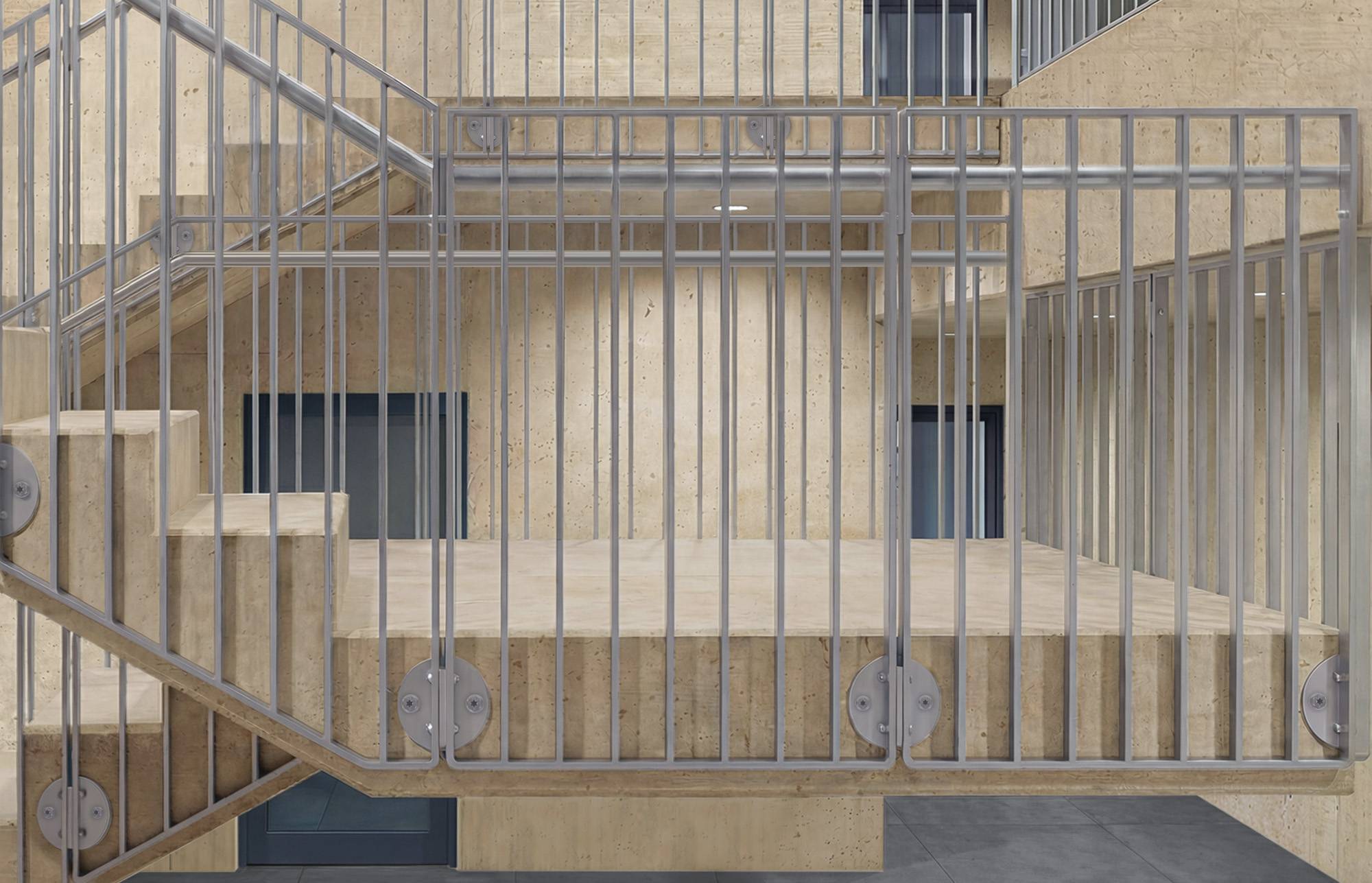 Ein Treppenhaus aus Beton und ein Treppenabsatz, umschlossen von grauen Metallgeländern und Sprossen, von der Seite in einem minimalistischen industriellen Gebäudeinneren betrachtet.