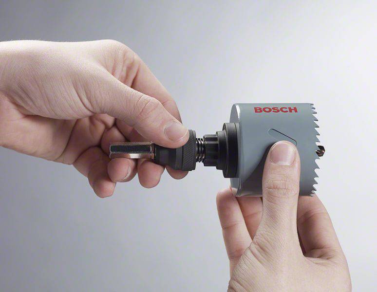 Hände montieren einen grauen Bohrkopf mit rotem 'Bosch'-Logo auf einem Metallaufsatz, vor neutralem Hintergrund.