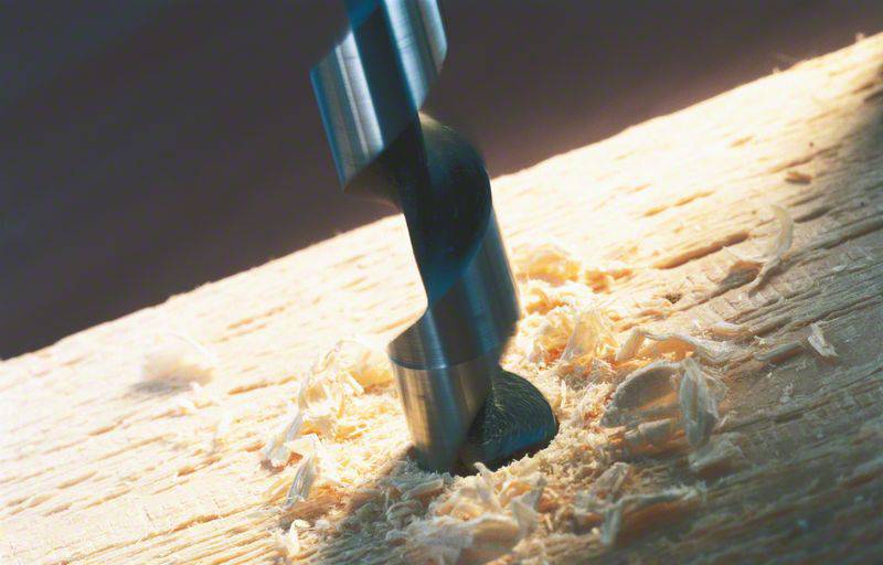 Ein Bohrer durchdringt ein Holzstück, umgeben von Holzspänen, in einem Lichtstrahl.