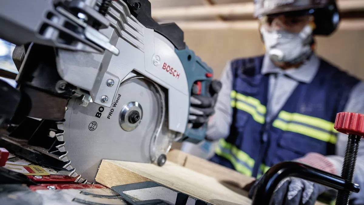 Arbeiter, der eine Kreissäge zum Holzschneiden verwendet und Sicherheitsausrüstung wie Handschuhe, Helm und Maske trägt.