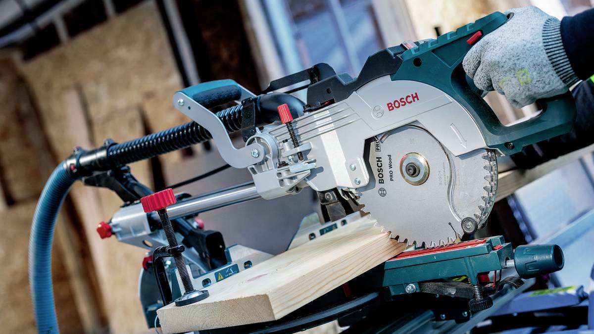 Eine Nahaufnahme einer Kreissäge, die durch ein Stück Holz schneidet, wobei Schutzhandschuhe an den Händen des Bedieners zur Sicherheit zu sehen sind.